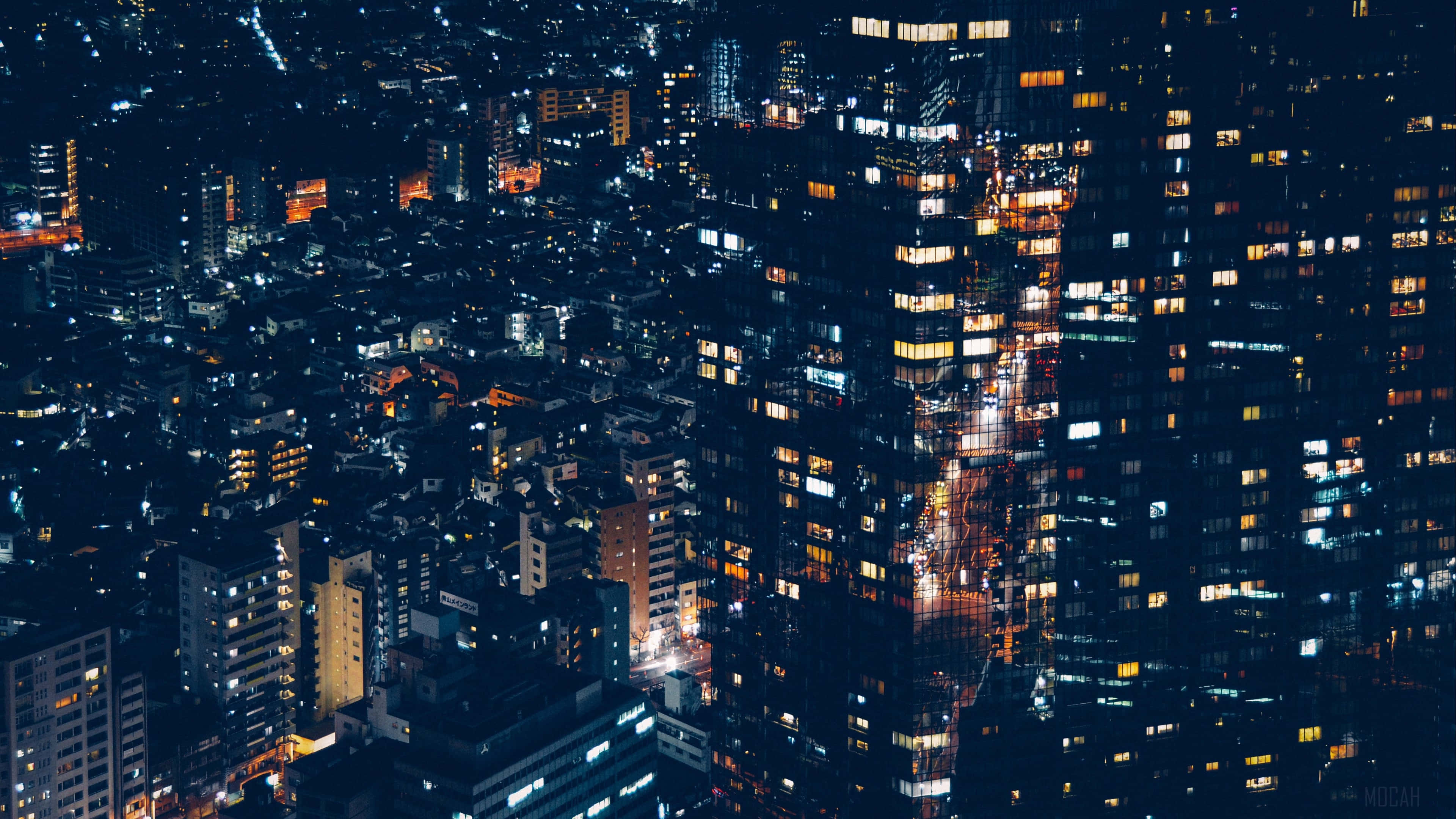 City Lights 桌布 壁紙 — 夜晚密集城市的鳥瞰圖，發光的窗戶和明亮的街道營造出充滿活力的城市掛毯。