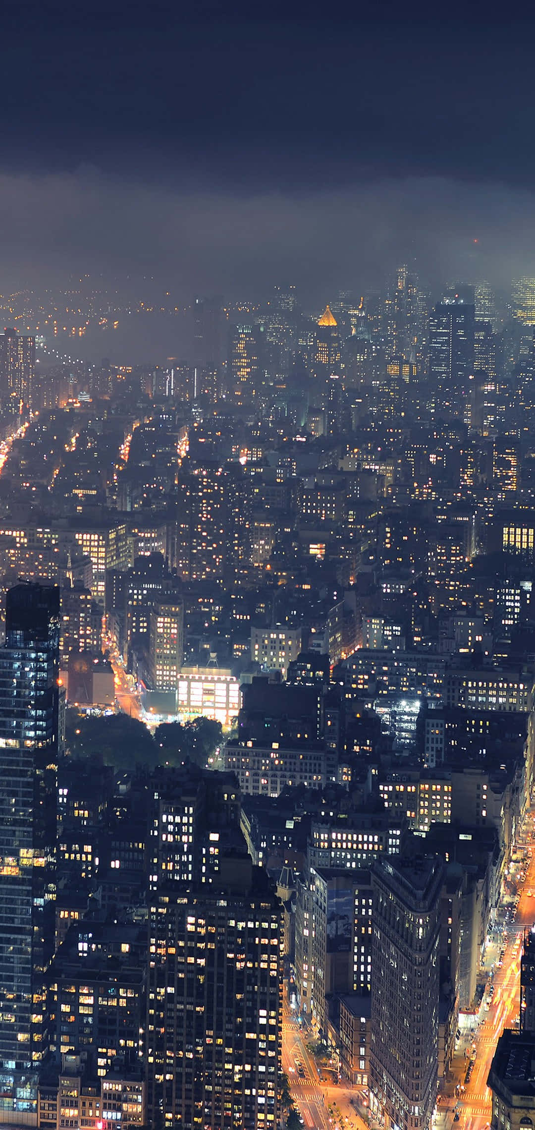 Panorama 桌布 壁紙 — 夜晚廣闊城市的鳥瞰圖，無數發光的窗戶和燈火通明的街道，在陰暗多雲的天空下。