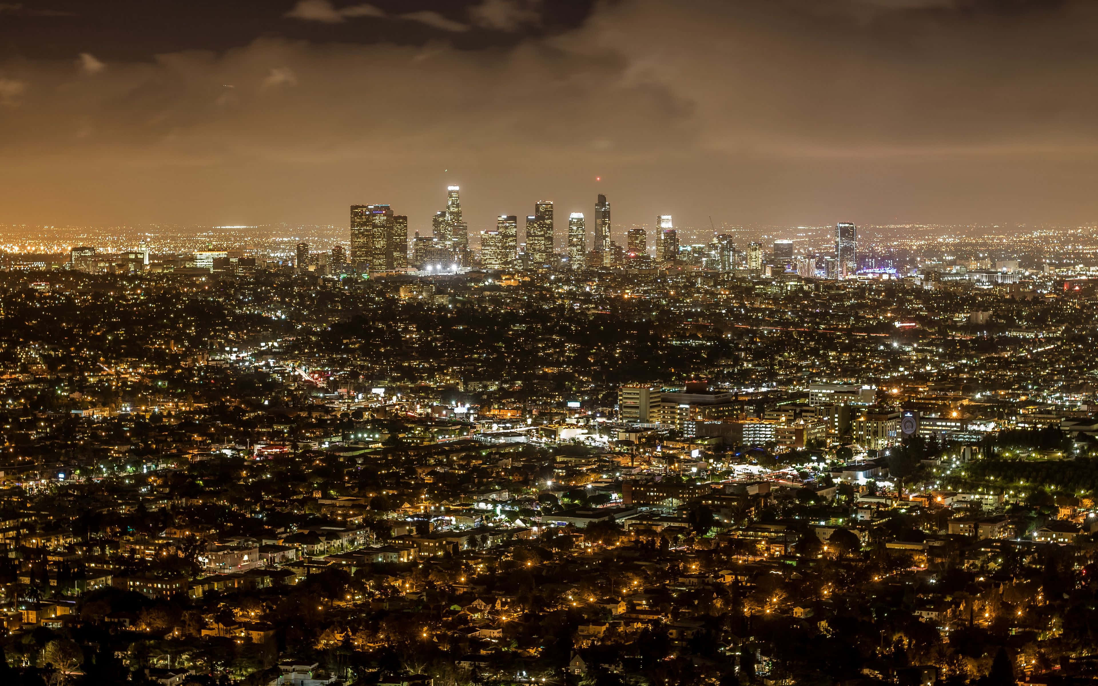 La 桌布 壁紙 — 夜晚廣闊的城市景觀，無數建築物和街道的燈光在陰雲密布的天空下閃爍。