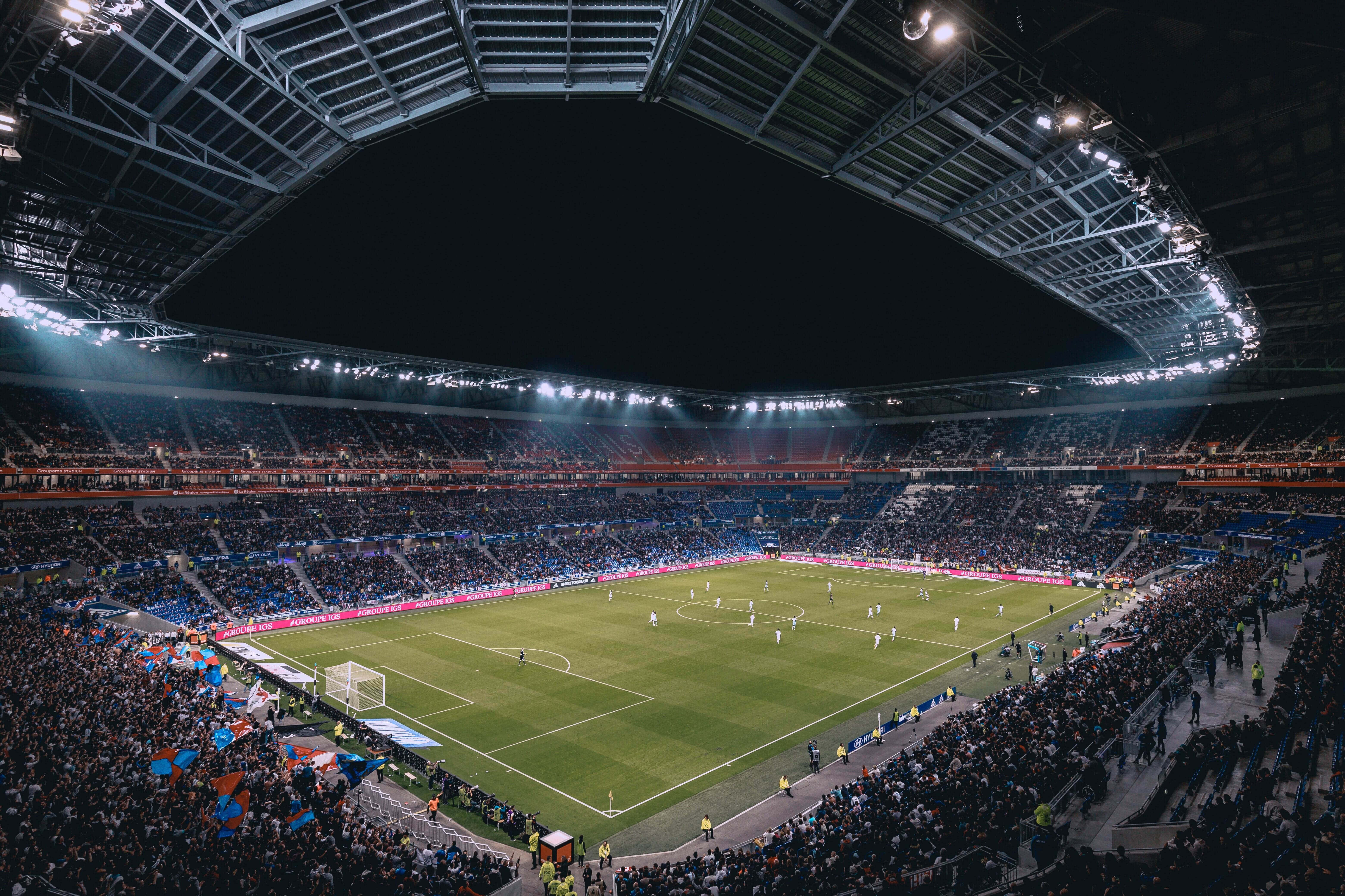Football Stadium 桌布 壁紙 — 夜晚擠滿觀眾的足球場鳥瞰圖，明亮的燈光照亮綠色球場和歡呼的球迷。