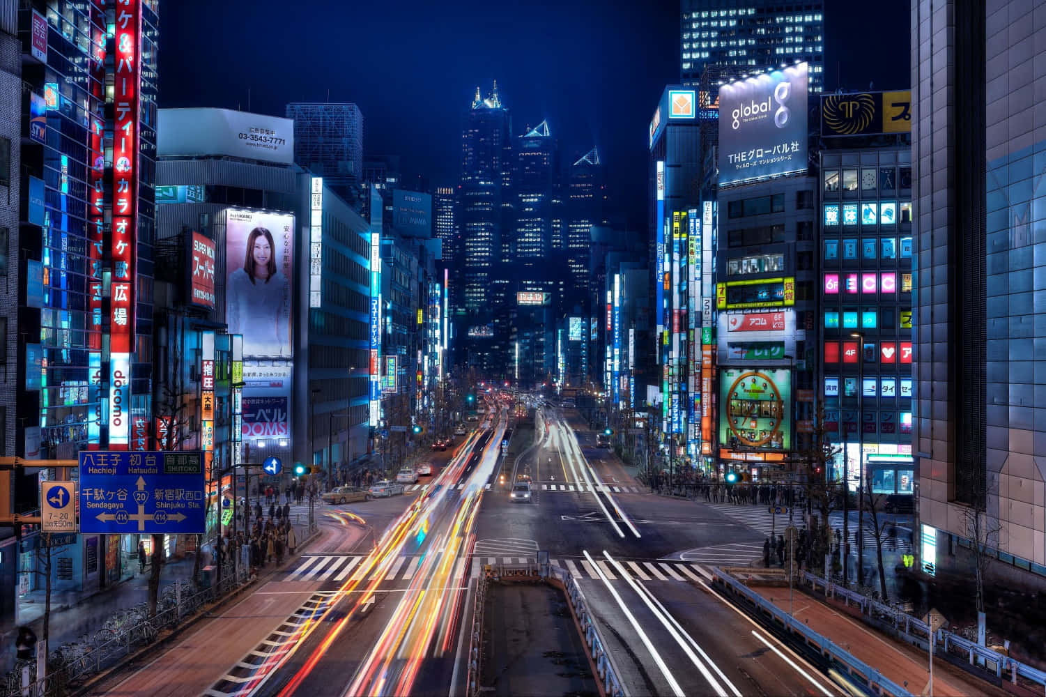 東京 桌布 壁紙 — 夜晚東京一條充滿活力的霓虹燈街道，車燈劃過，高聳的摩天大樓在黑暗的天空下閃耀。