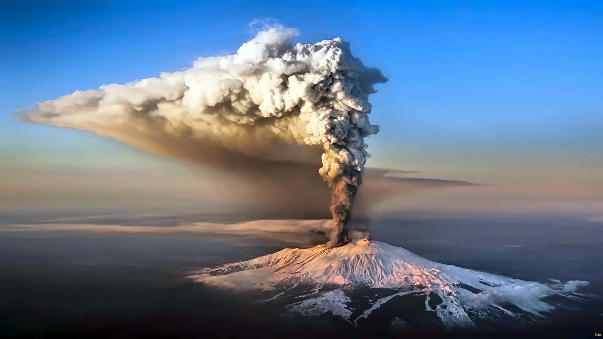 一座白雪覆蓋的火山噴發，巨大的火山灰雲升入日出時的天空。