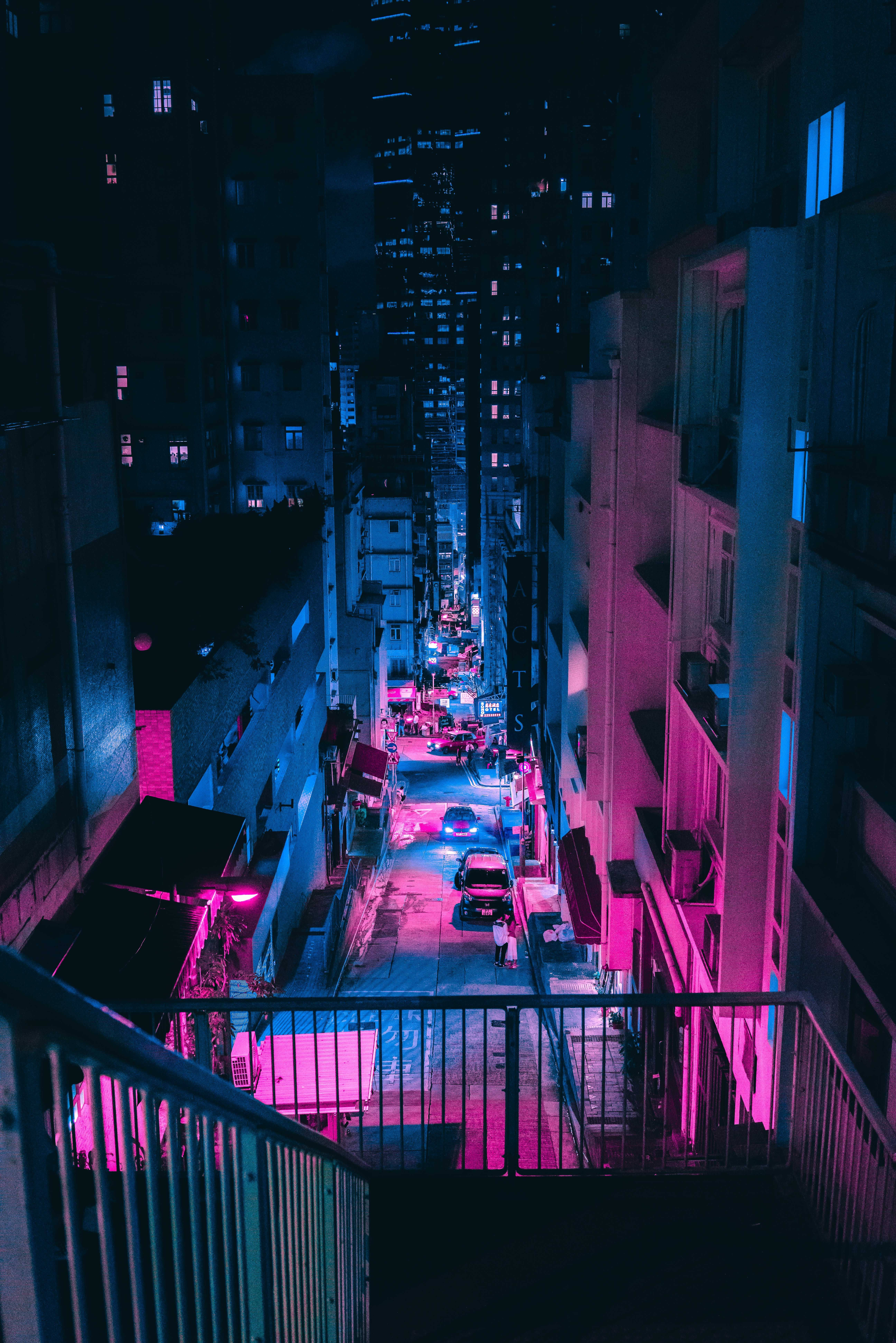 google 桌布 壁紙 — 夜晚狹窄的城市小巷，沐浴在鮮豔的粉紅色和藍色霓虹燈光中，反射在潮濕的路面上。