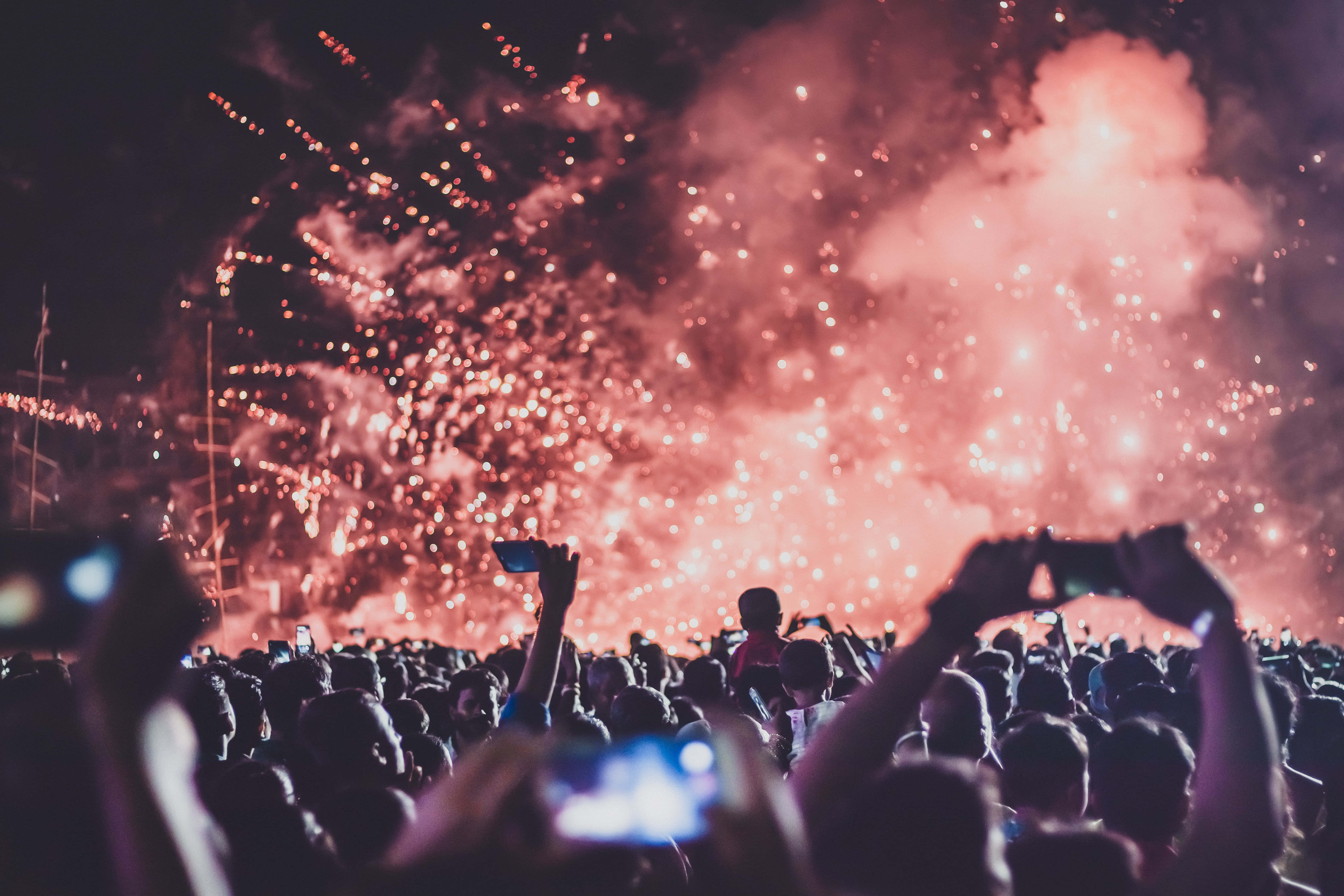 music festival 桌布 壁紙 — 夜晚的人群舉起手機捕捉頭頂上綻放的耀眼紅色煙花。