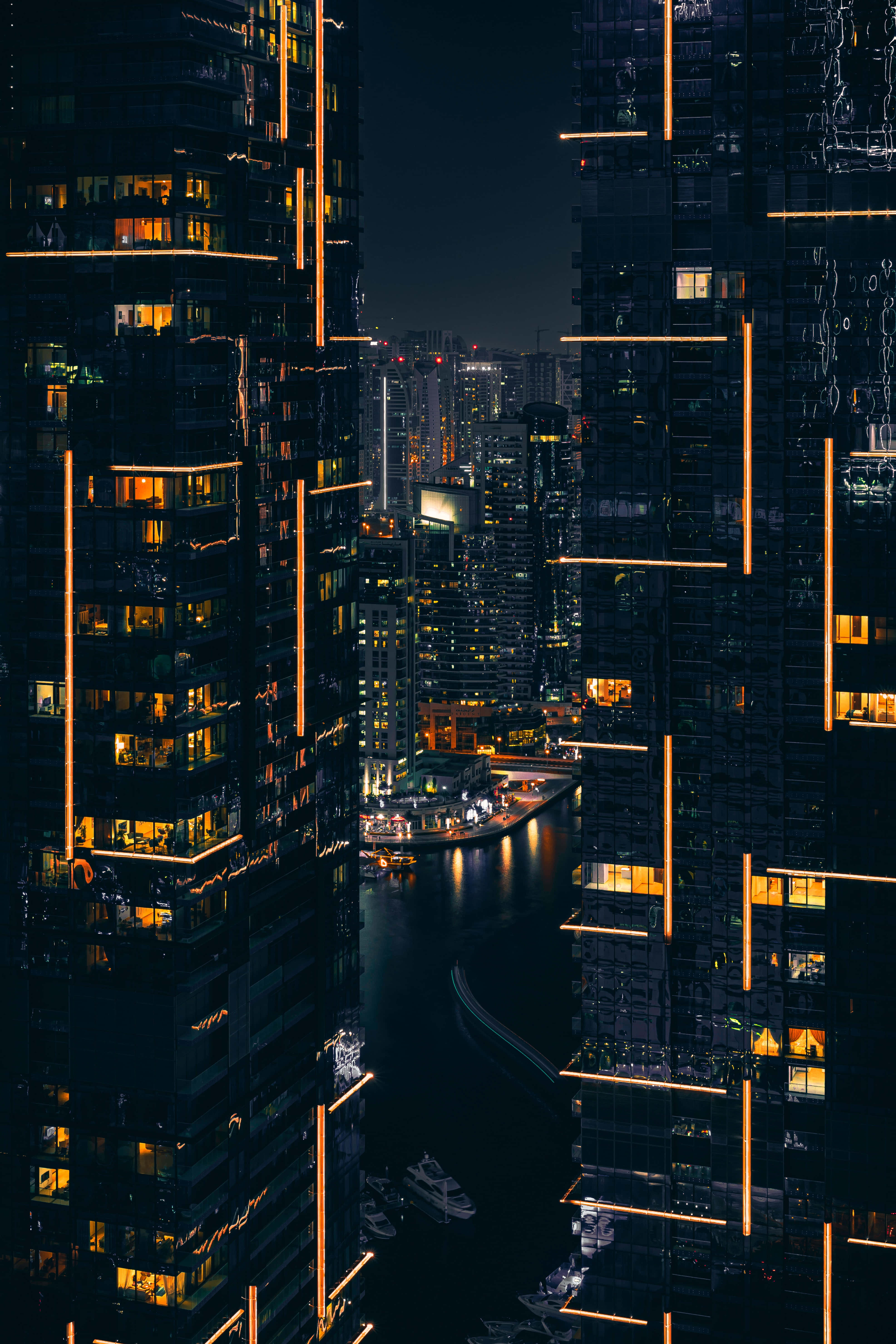 深色主題 桌布 壁紙 — 夜晚的城市景觀，高聳的摩天大樓沿著蜿蜒的水道散發著溫暖的光芒。