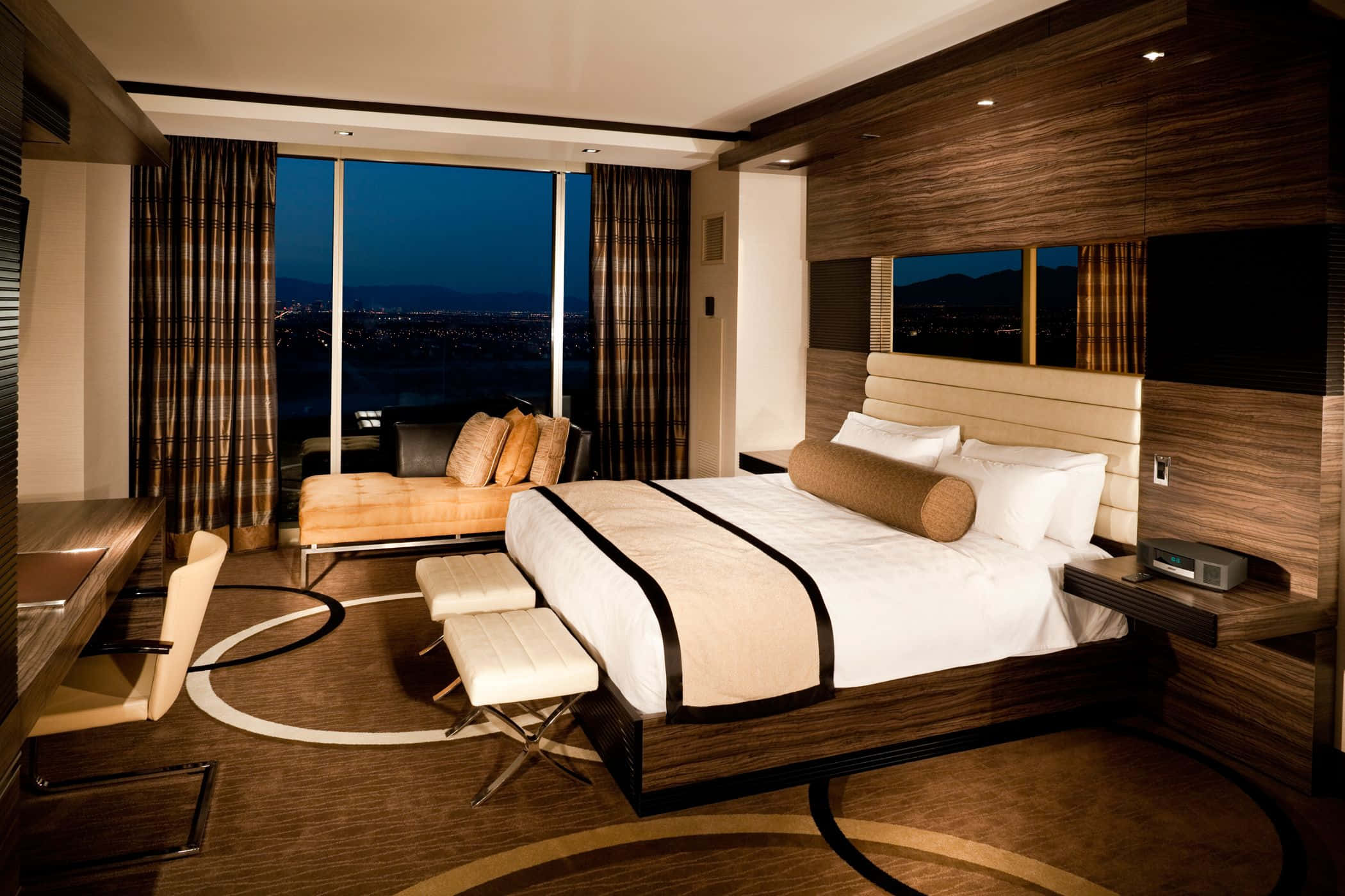 Hotel Room 桌布 壁紙 — 夜晚的豪華酒店客房，配有大床、城市景觀和溫暖的木質裝飾。