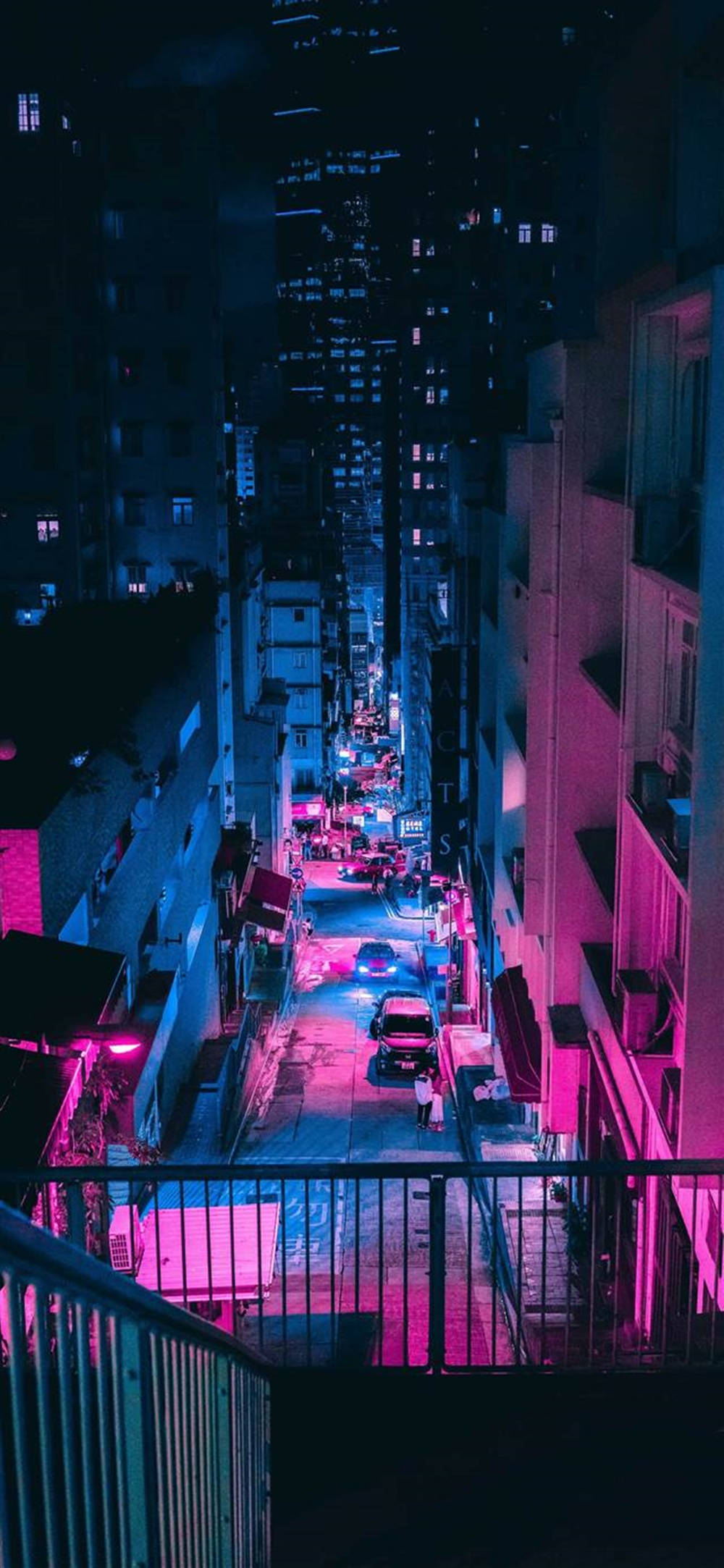 Device 桌布 壁紙 — 夜晚的都市小巷，被霓虹燈淹沒，粉紅色和藍色的燈光在高聳建築物之間的濕漉漉路面上反射。