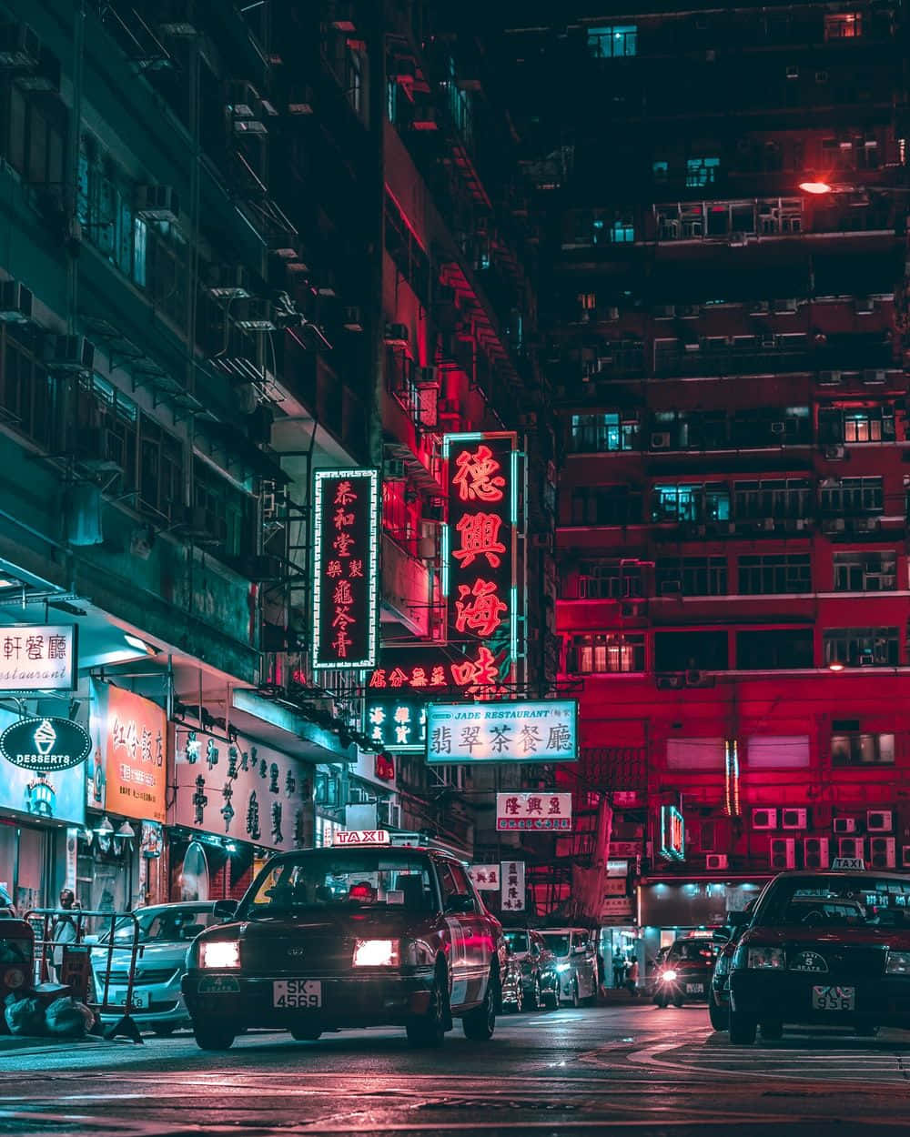 壁紙 — 夜晚的霓虹燈城市街道，高聳的建築物、發光的紅色和藍色招牌，以及濕漉漉的路面上反射出鮮豔燈光的的士。