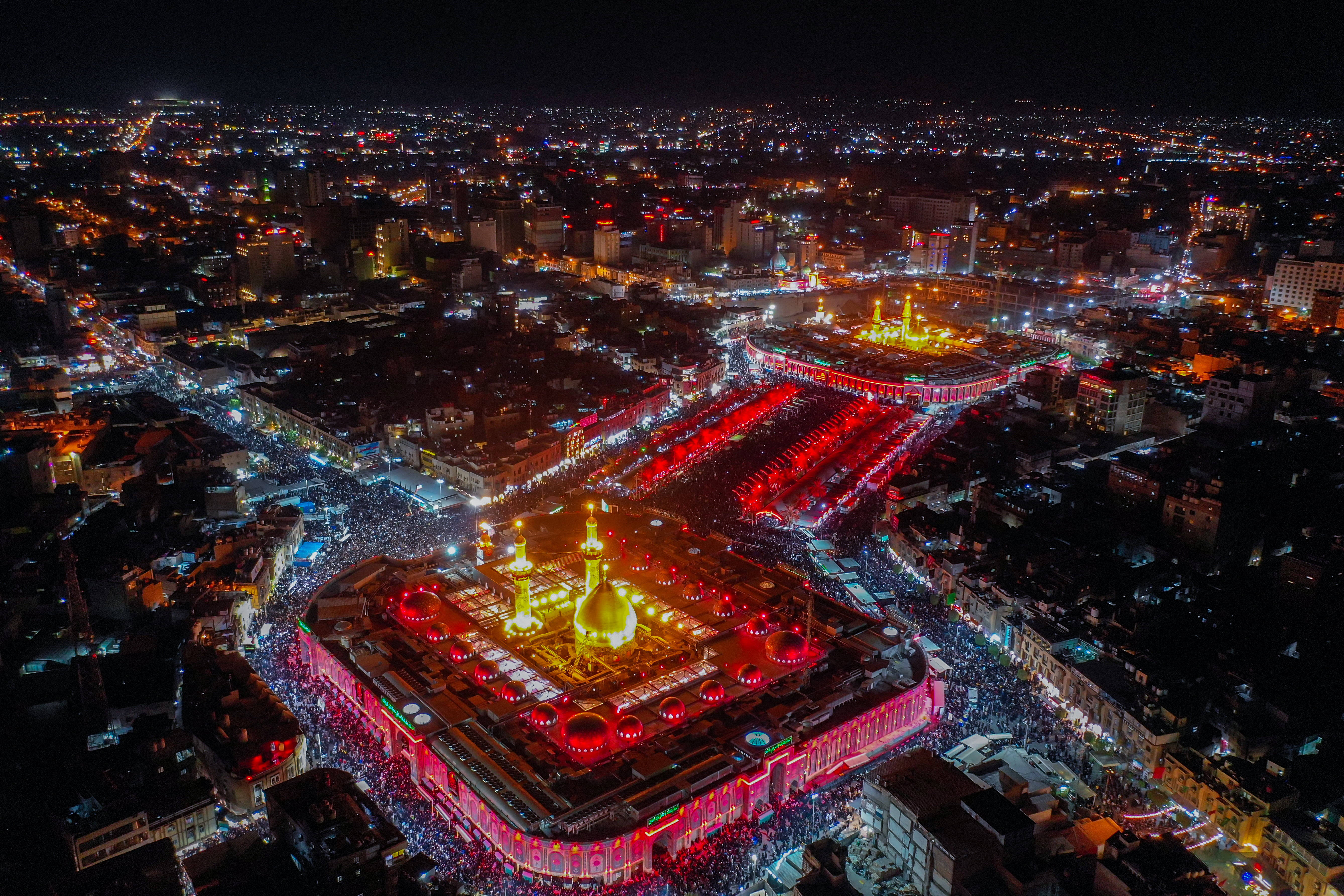 Karbala 桌布 壁紙 — 夜晚空中俯瞰一個被人群和閃爍城市燈光包圍的大型照明宗教建築群。