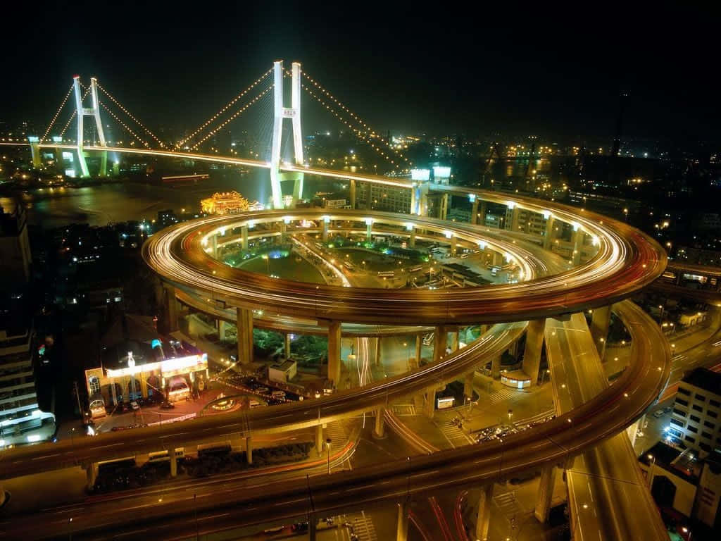 Mumbai 桌布 壁紙 — 夜晚空中俯瞰發光的螺旋形高速公路交匯處，位於水上吊橋下方，城市燈光閃爍。