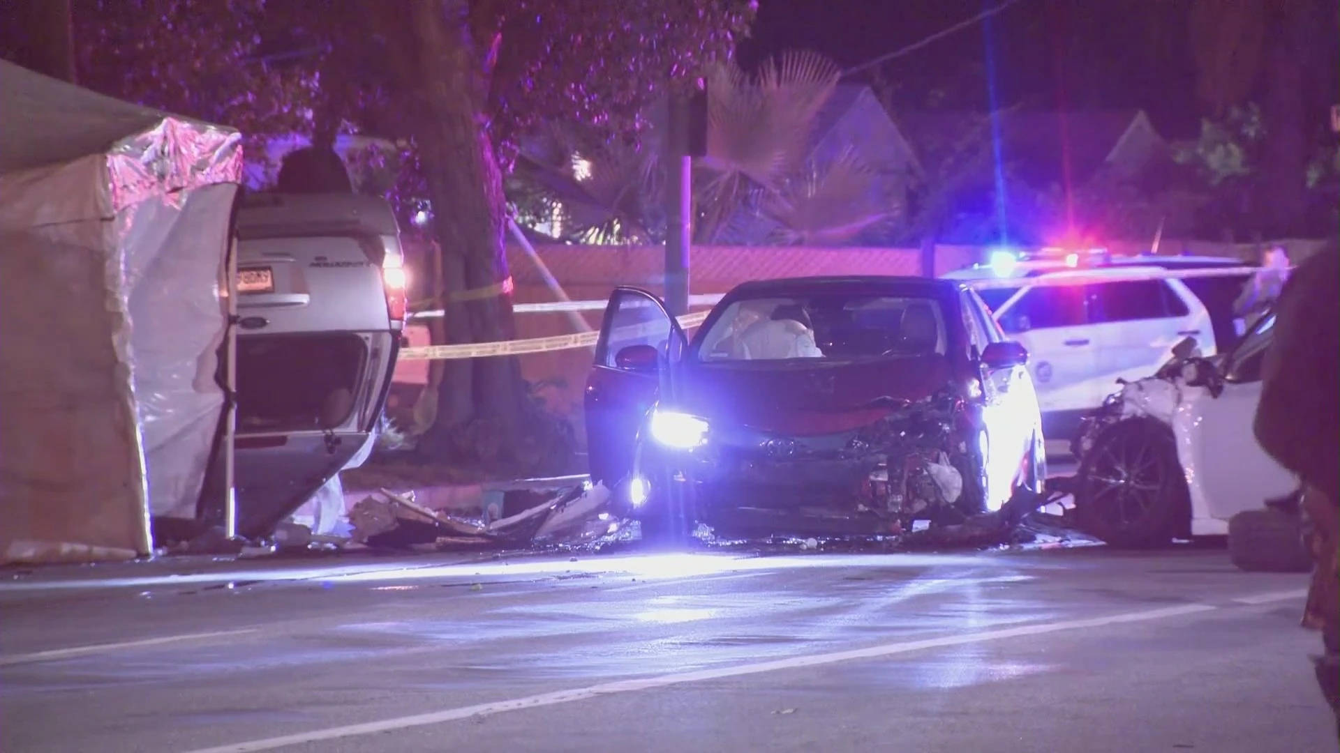 Car Accident 桌布 壁紙 — 夜晚街景，有撞毀的汽車、閃爍的警燈，以及圍繞著損毀車輛的封鎖膠帶，在人工照明下。