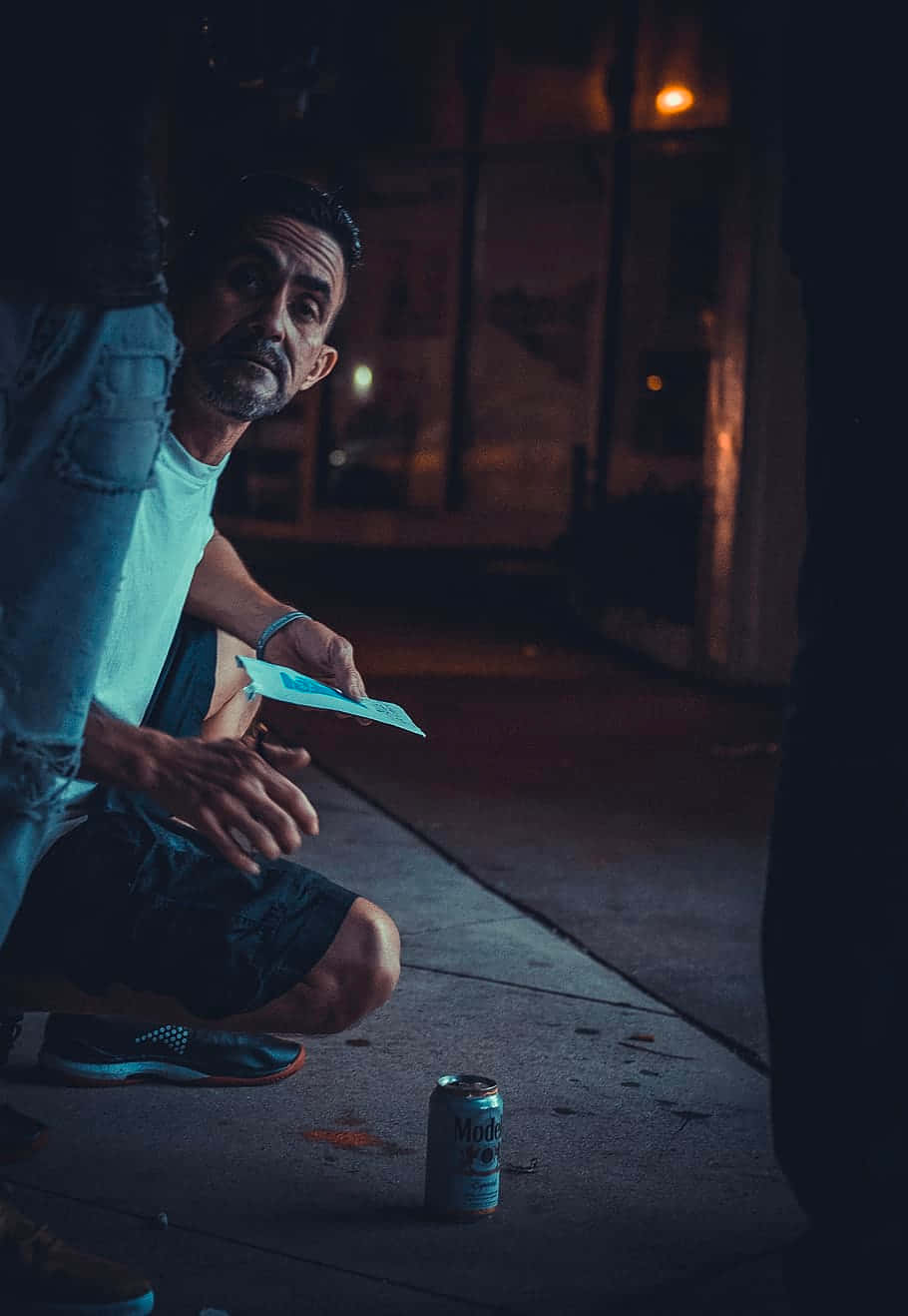一名男子在夜晚的行人道上跪下，在啤酒罐旁手持傳單。