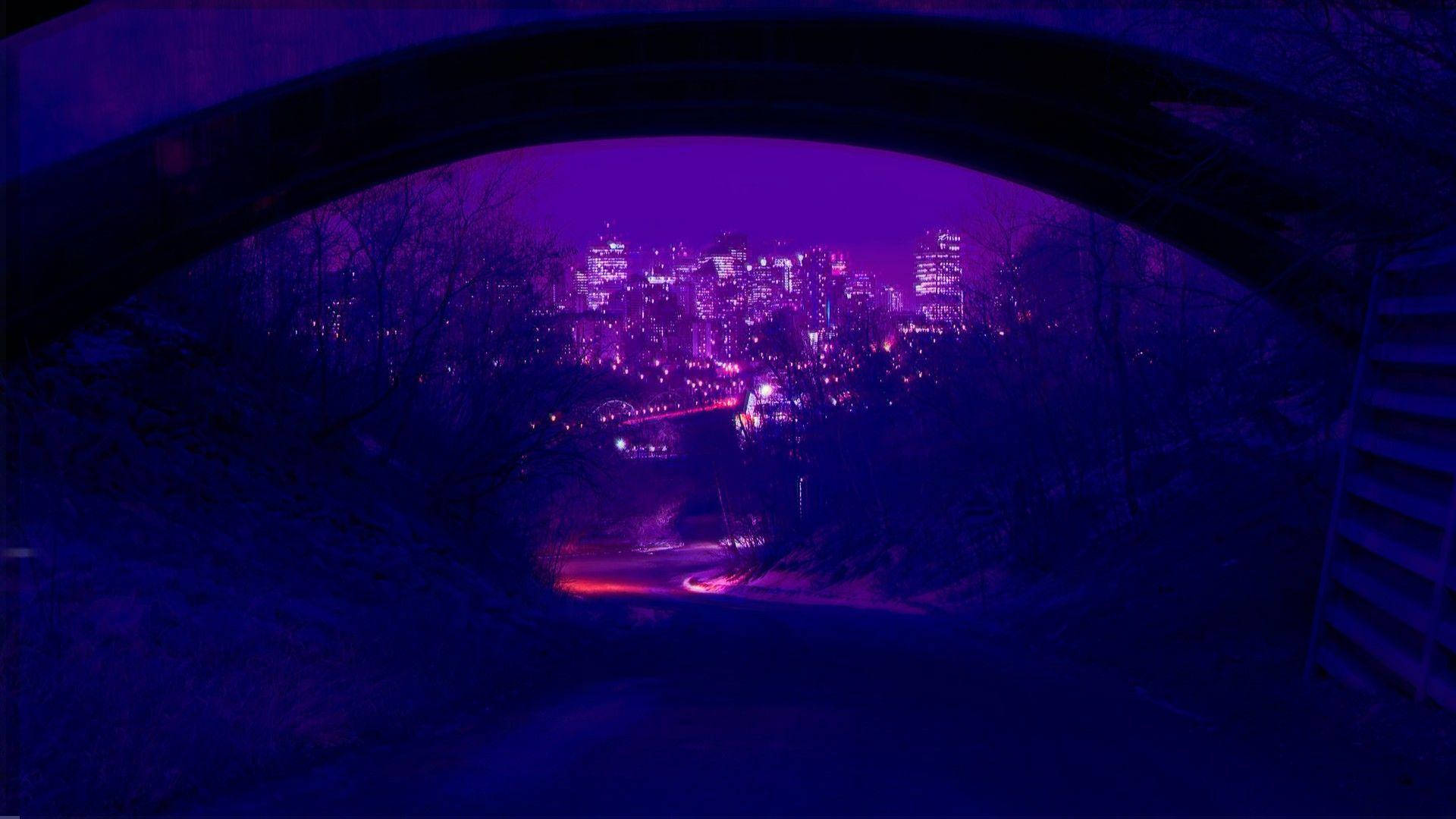 View 桌布 壁紙 — 夜晚透過黑暗拱門看到的紫色調城市景觀，帶有發光的燈光和光禿的樹木。