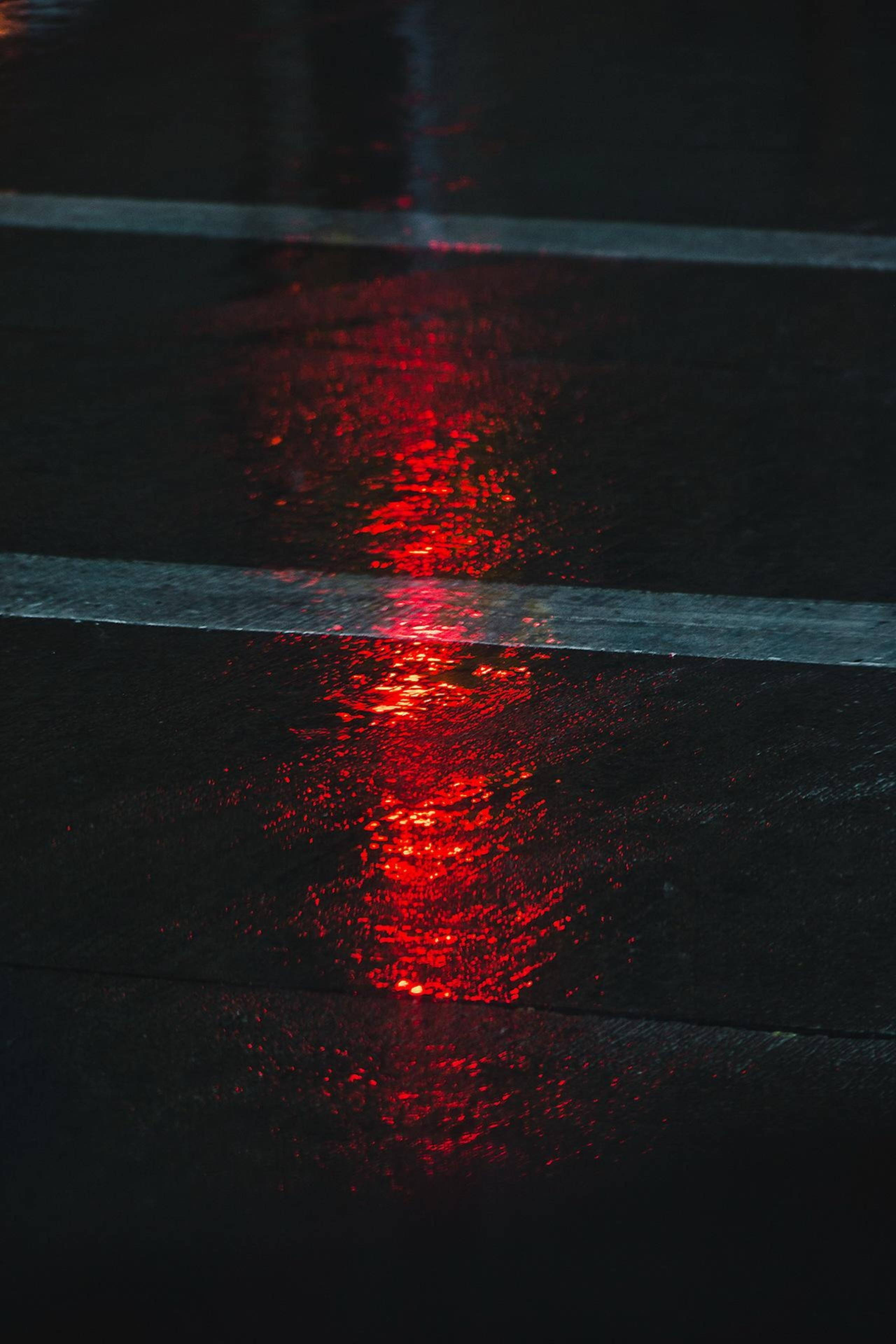 霓虹美學 桌布 壁紙 — 夜晚雨水濕滑的路面特寫，反射出汽車煞車燈的鮮豔紅光。