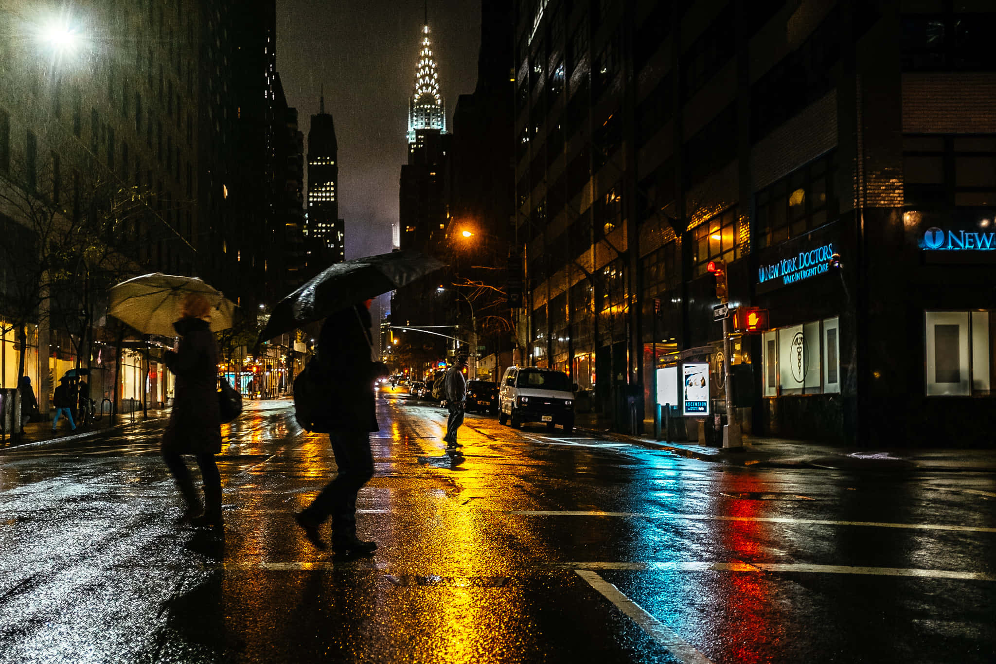 Night Street 桌布 壁紙 — 夜晚雨濕的城市街道，行人撐傘，倒映著高聳摩天大樓的霓虹燈光。