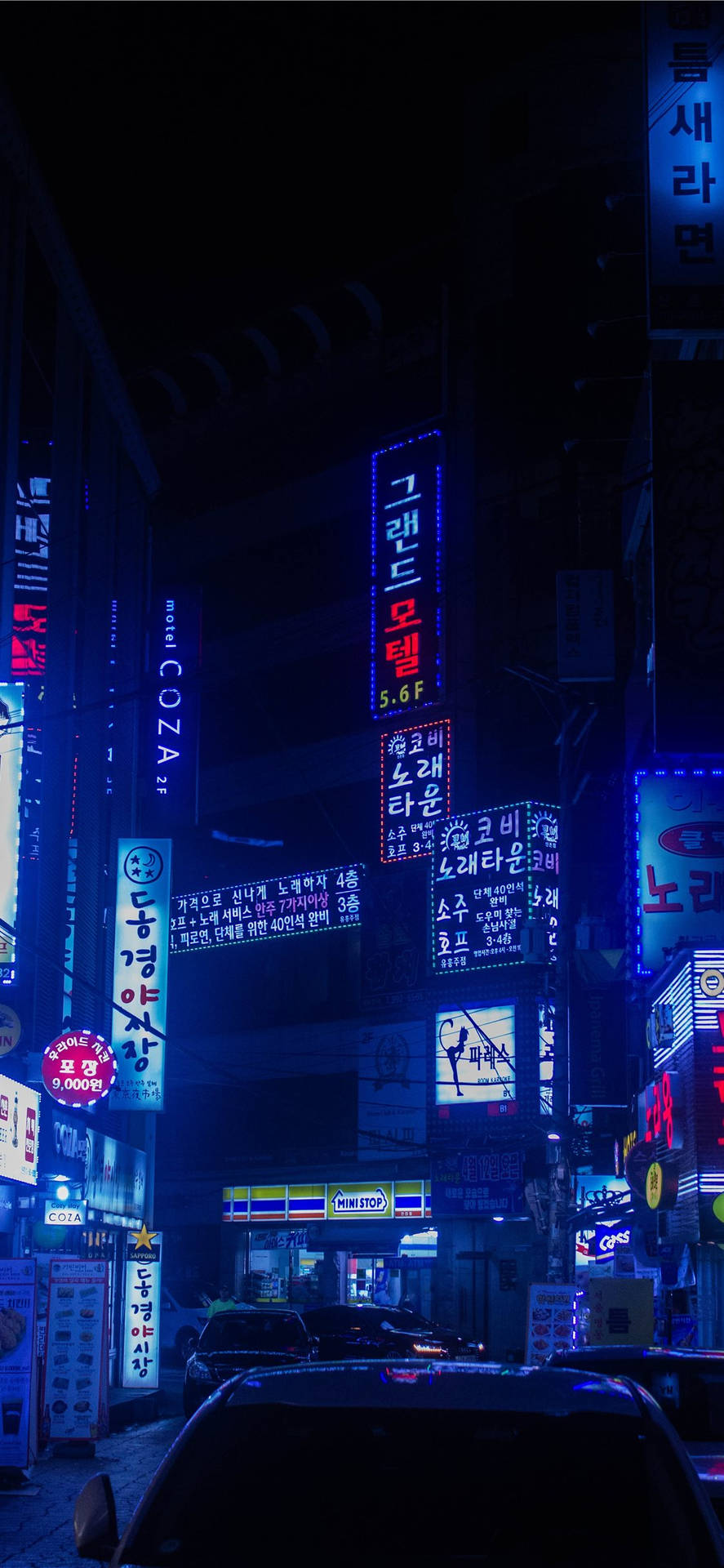 霓虹招牌照亮夜晚濕滑嘅街道，有泊車同韓文字。