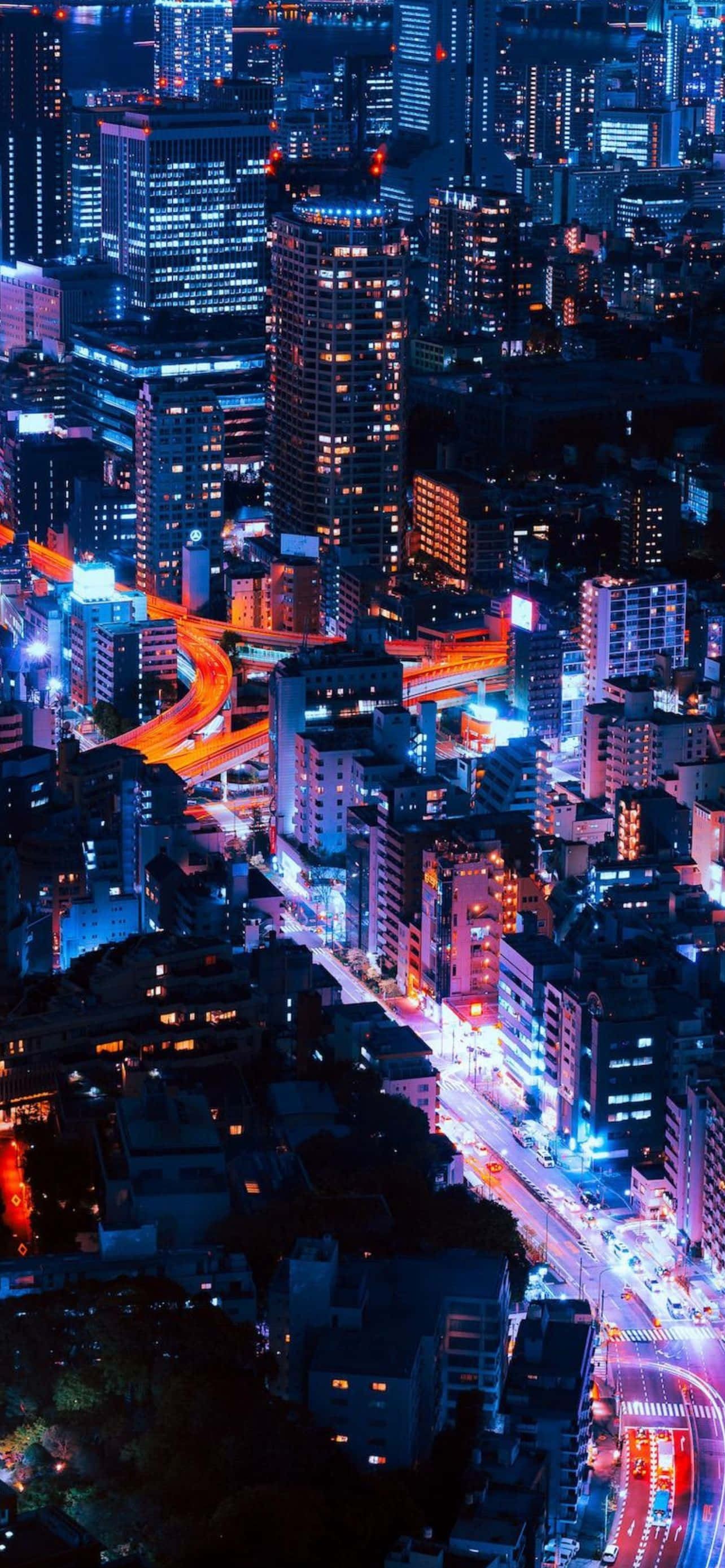 型格 iPhone 壁紙 桌布 壁紙 — 夜晚霓虹燈照亮城市景觀的鳥瞰圖，閃爍的摩天大樓和充滿活力的交通痕跡。