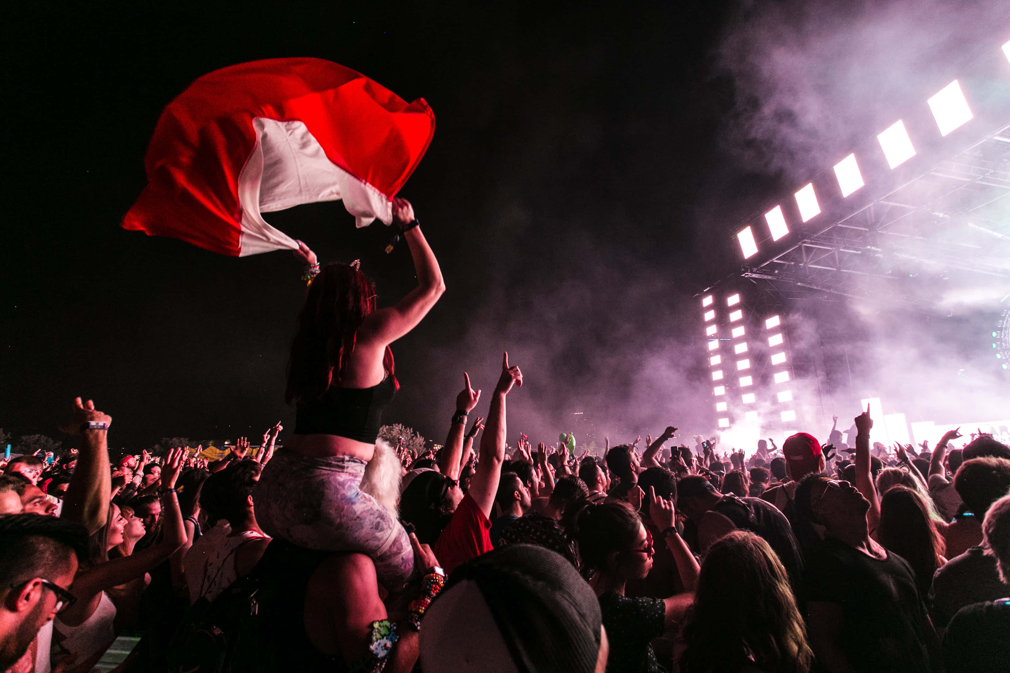 music festival 桌布 壁紙 — 夜晚音樂會的人群，有人在明亮的舞台燈光下在人群上方揮舞紅白旗幟。