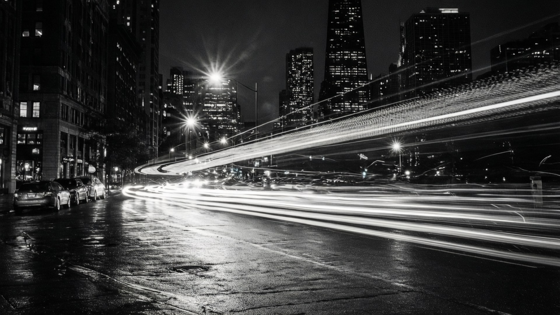 黑白夜間城市街道，帶有汽車燈光軌跡和高樓大廈