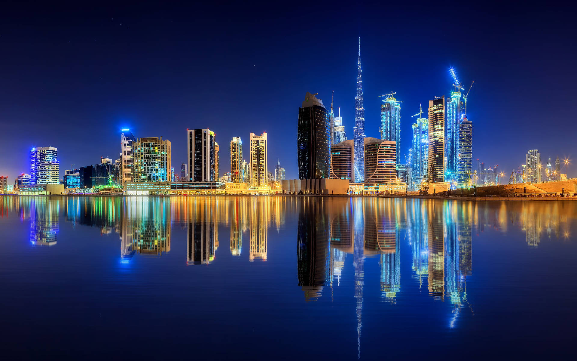 夜景城市燈光的迷人畫面 壁紙 — 杜拜令人目眩的夜景，摩天大樓閃爍著藍色和金色，完美倒映在平靜的水面上。