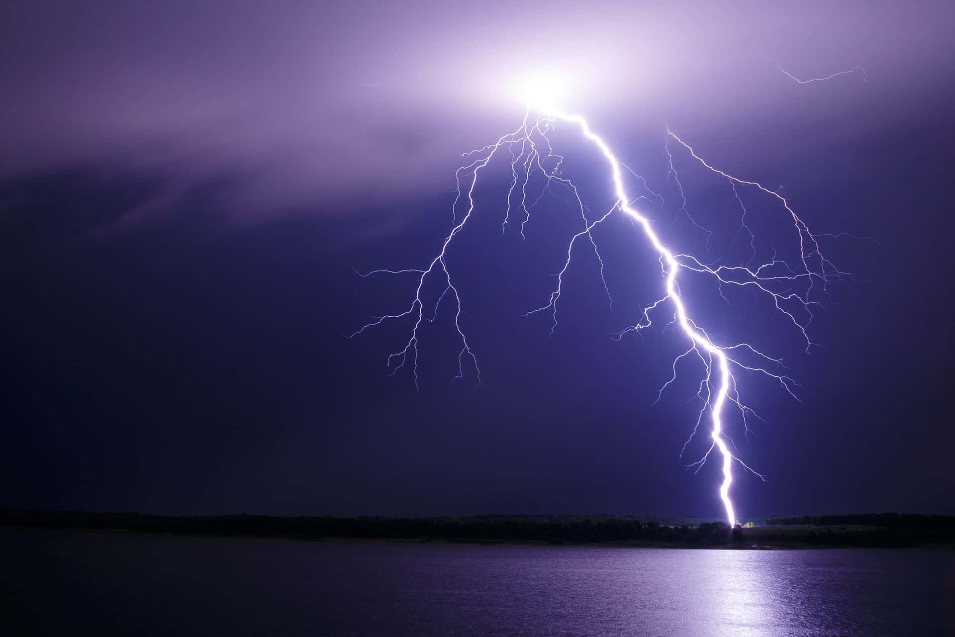 閃電在暴風雨的夜空下照亮黑暗的湖泊。