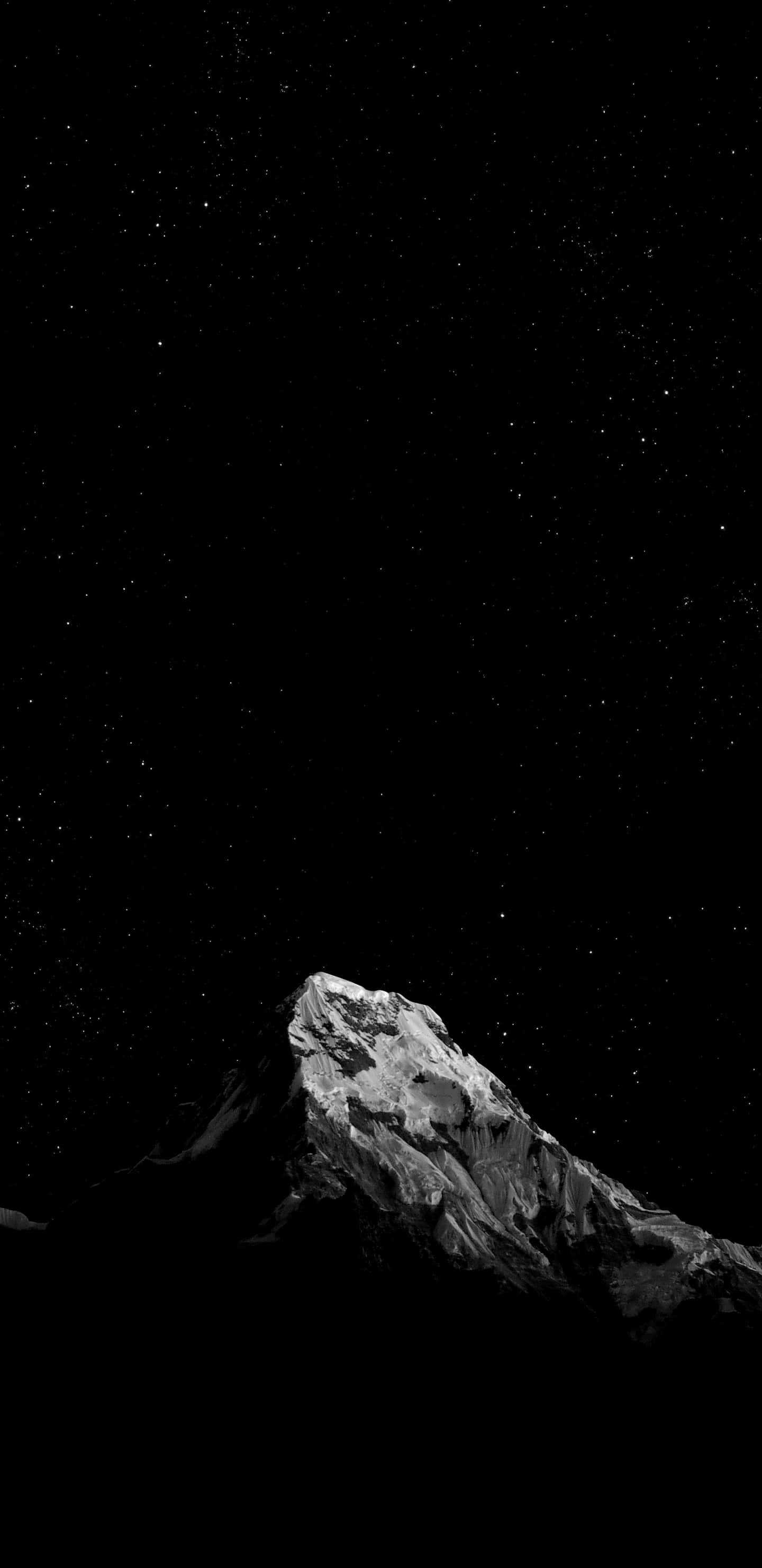 夜空中的一座山 壁紙 — 一座白雪覆蓋的山峰在繁星點點的夜空下以高對比黑白呈現。