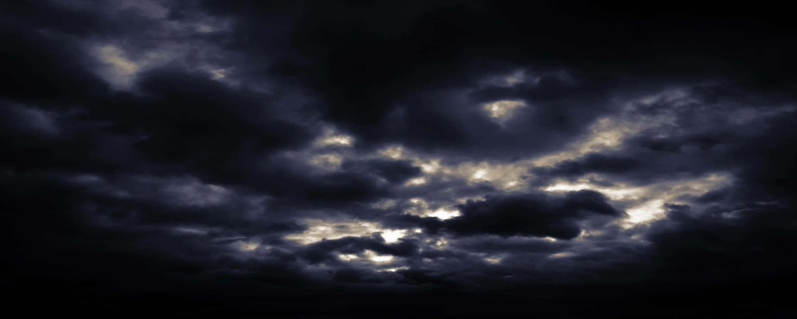 夜空中的烏雲密布 壁紙 — 戲劇性的烏雲在黑色天空中旋轉，邊緣閃耀著金色光芒。