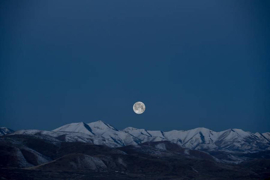 夜空中輝煌的滿月 壁紙 — 一輪滿月在深藍色暮色天空下照耀著積雪覆蓋的山脈。