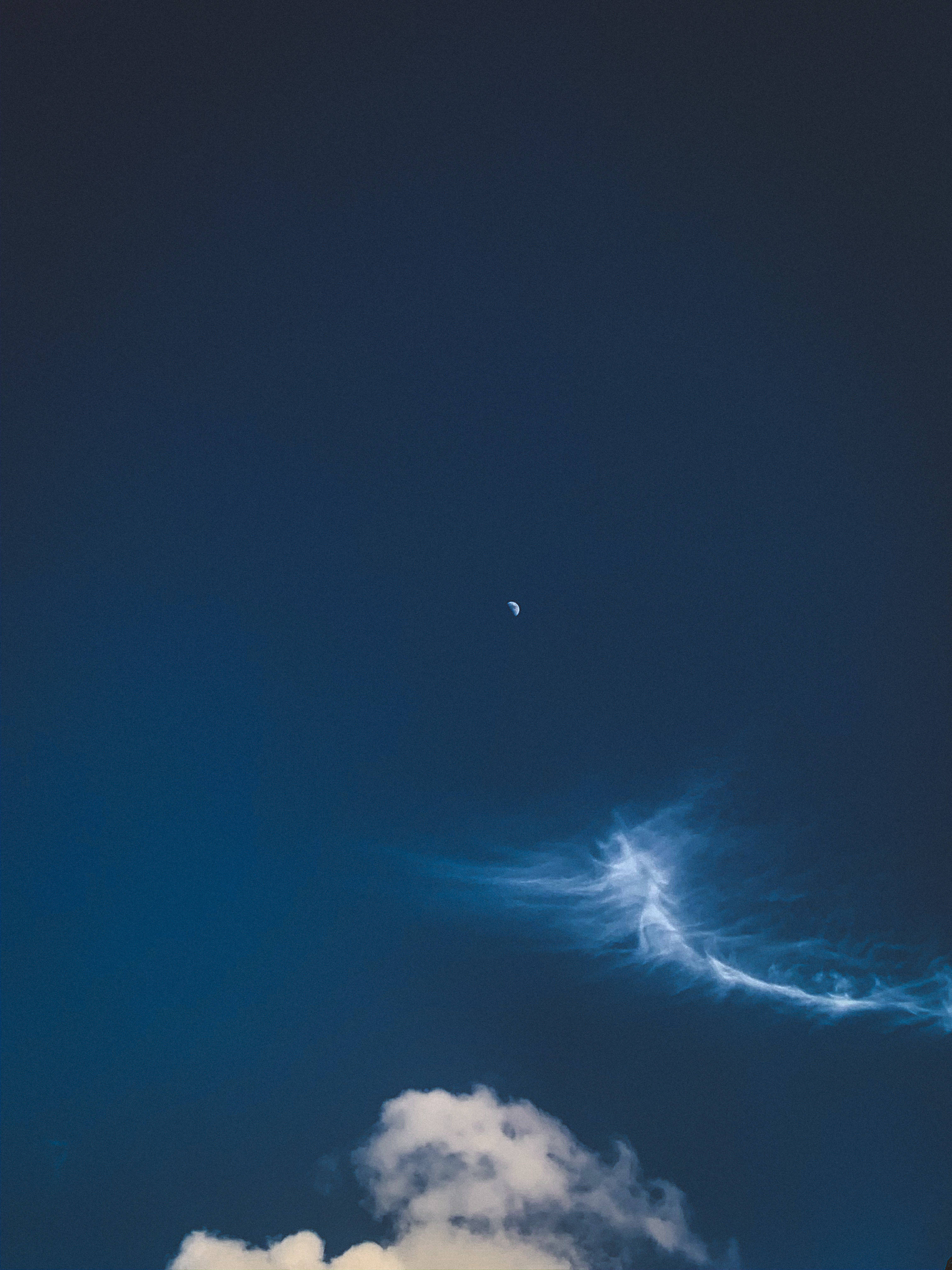 夜空獨特 iPhone 壁紙 — 一彎新月在深藍色暮色天空中的縷縷雲層上方閃耀。