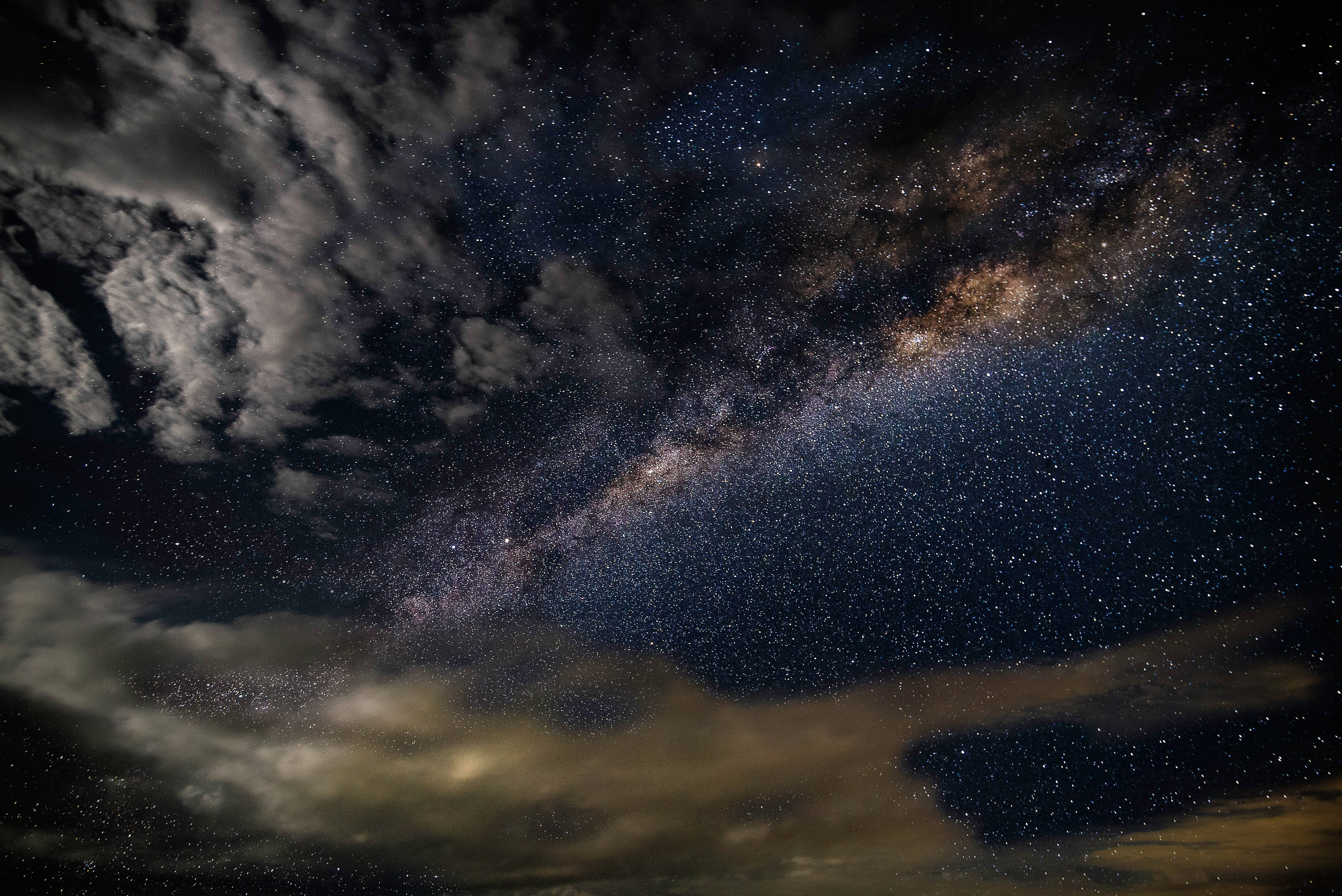 夜空螢幕保護 壁紙 — 令人嘆為觀止的銀河系景觀，橫跨繁星點點的夜空，下方有戲劇性的雲層。