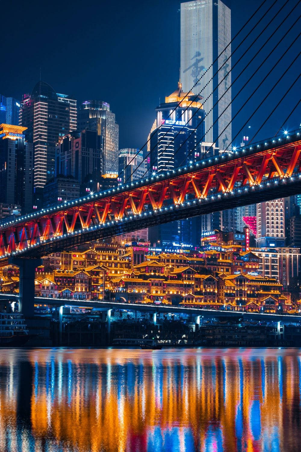 夜色下的重慶雙河橋PFP 壁紙 — 充滿活力的夜景城市景觀，一座發光的紅色橋樑橫跨河流，倒映著現代摩天大樓和傳統建築的霓虹燈光。