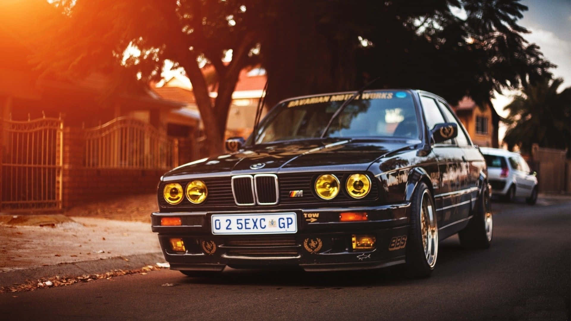 日落時分，一輛帶黃色車頭燈的黑色BMW E30停在住宅街道上。