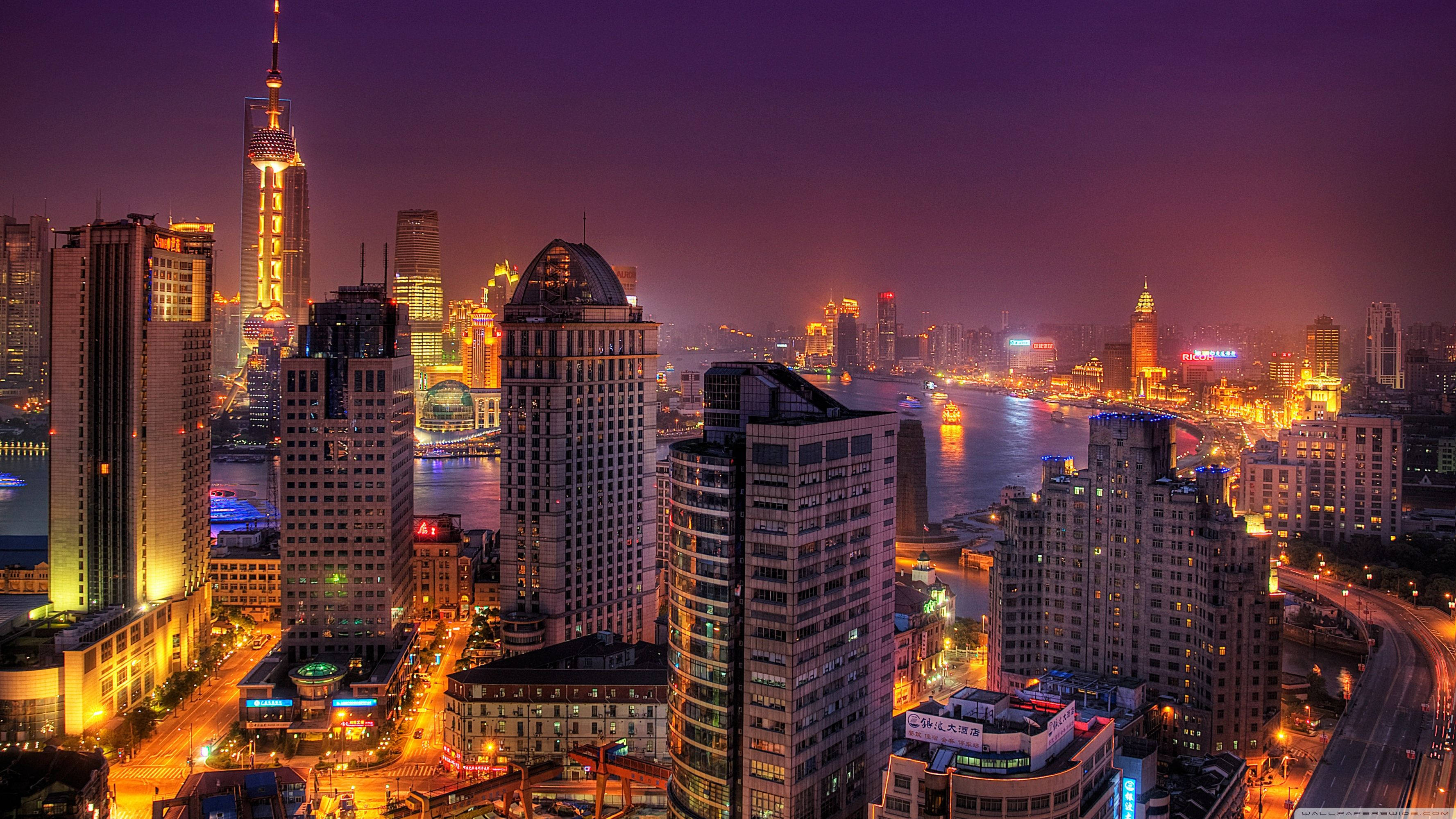 夜色中的現代上海 壁紙 — 充滿活力的夜景城市景觀，高聳的摩天大樓在深紫色天空下閃耀，下方是繁忙的河流。