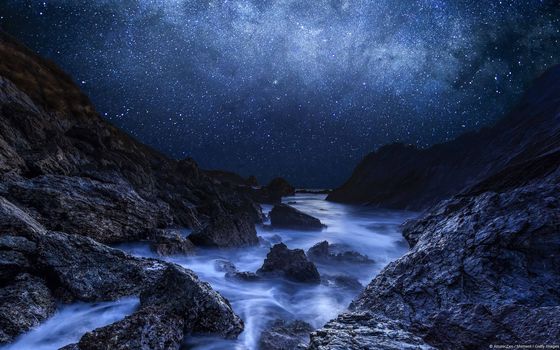 岩石海岸線上的星空夜空，帶有發光的藍色海洋波浪。