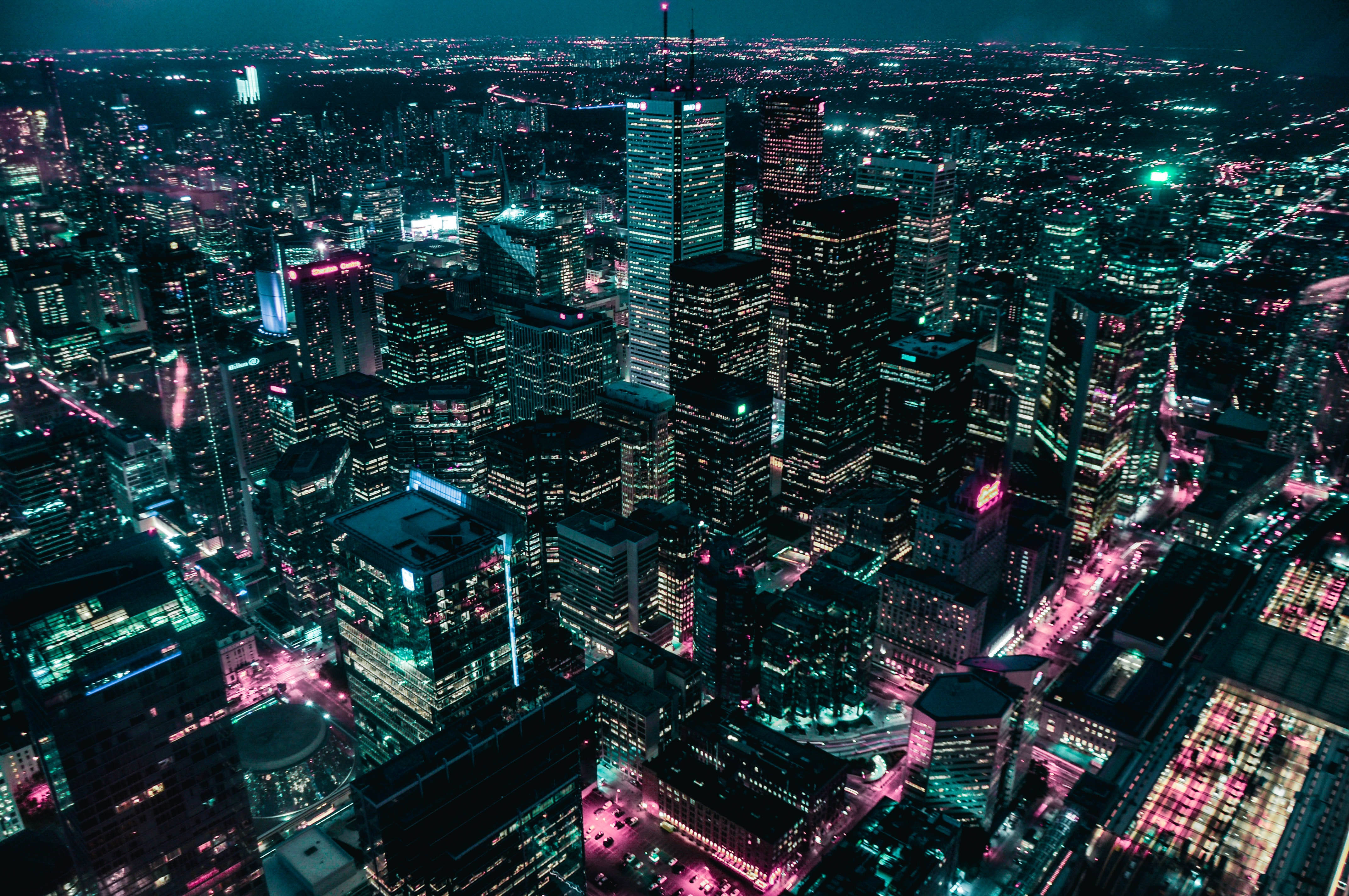 夜色中的紐約市霓虹光輝 壁紙 — 夜晚霓虹燈照亮城市景觀的鳥瞰圖，高聳的摩天大樓閃爍著青綠色和洋紅色調。