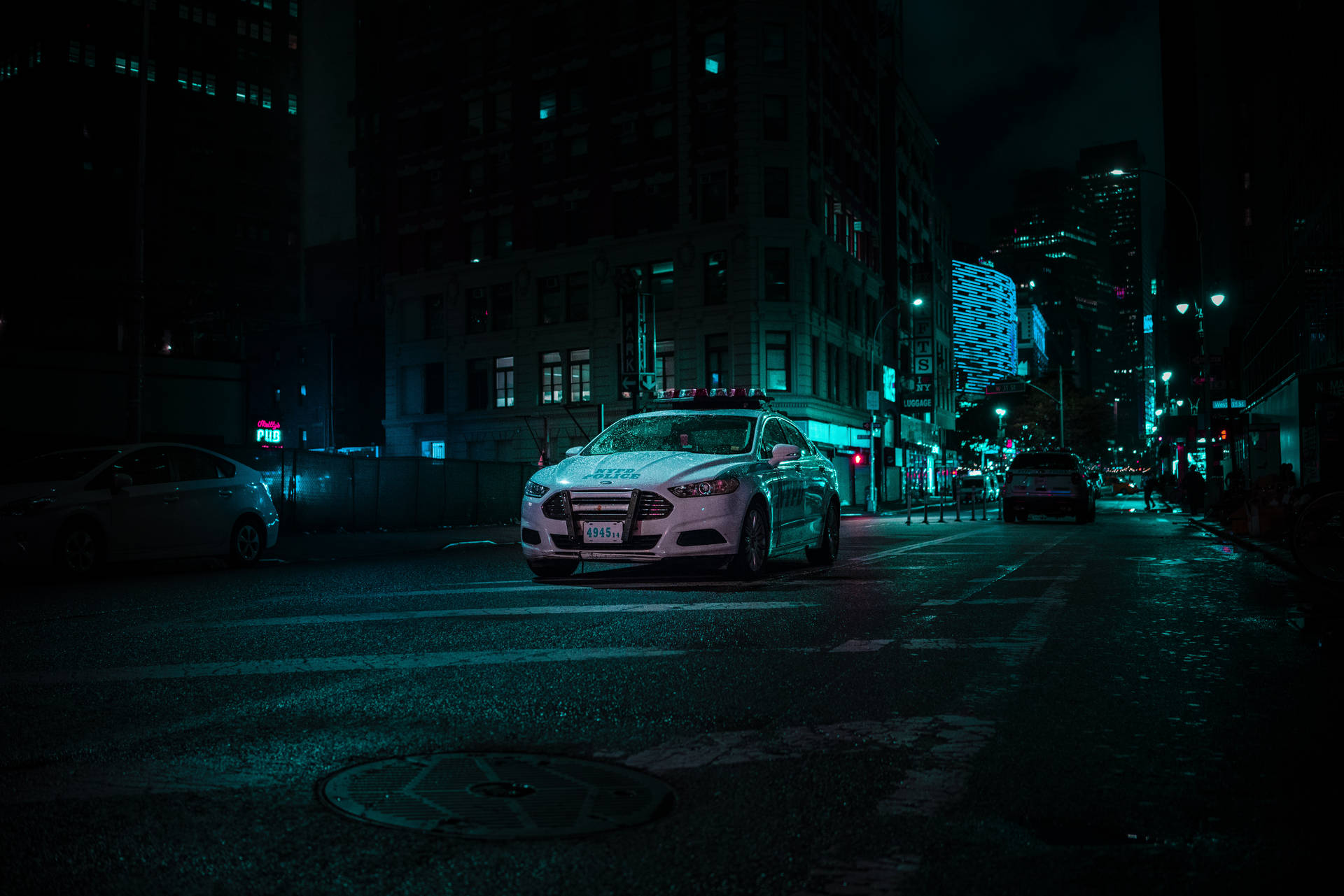 警車在夜間停泊在濕漉漉的城市街道上，霓虹燈光下。
