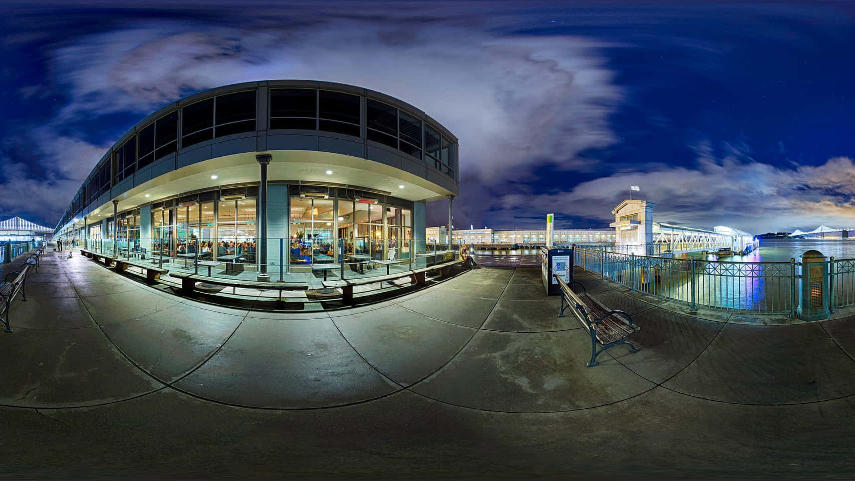 夜色海景 360度全景圖 壁紙 — 星空下，沿著海濱長廊的現代玻璃幕牆建築的全景夜景，設有長椅和欄杆。