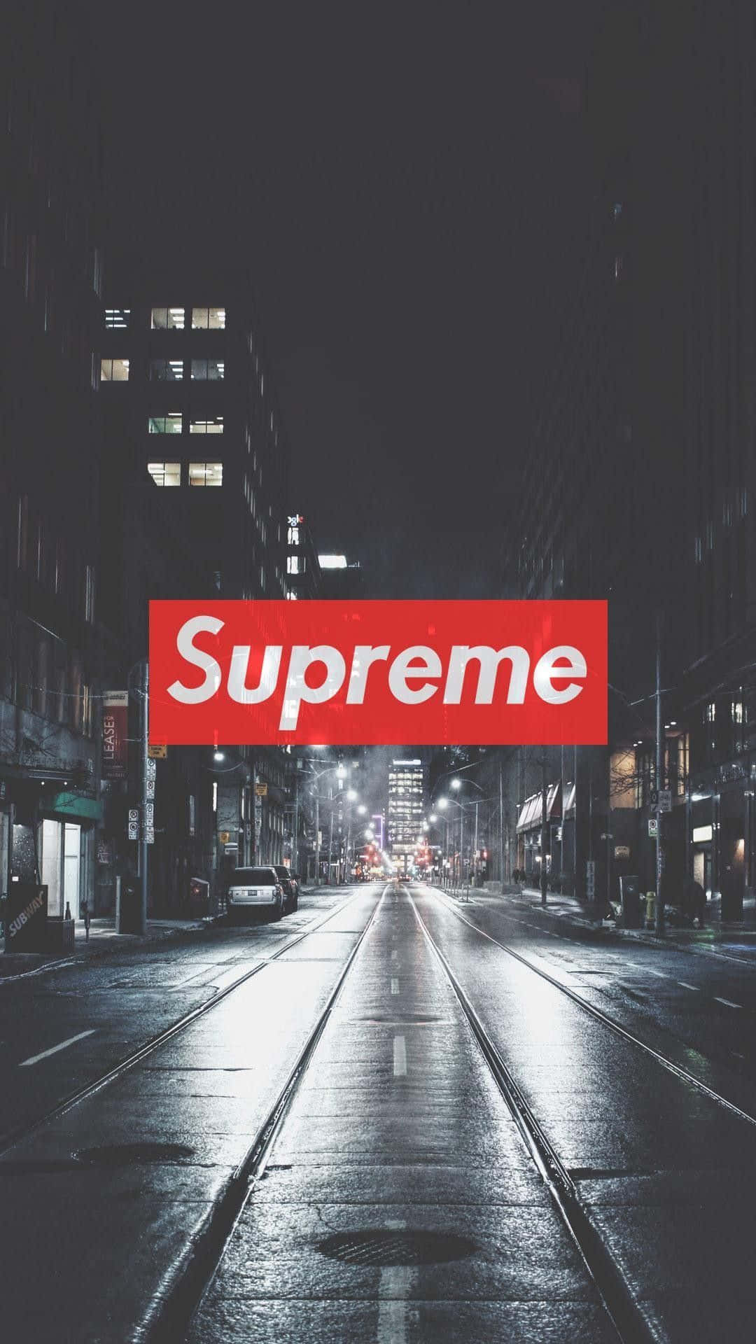 高樓之間夜晚濕漉漉的城市街道上方的紅色Supreme標誌。