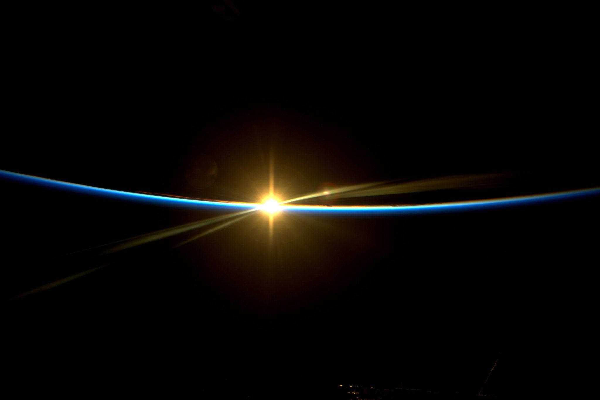 夜色霓虹黃燈 壁紙 — 燦爛的太陽光芒穿透地球地平線的曲線，在太空的虛空中投射出發光的藍色大氣邊緣。