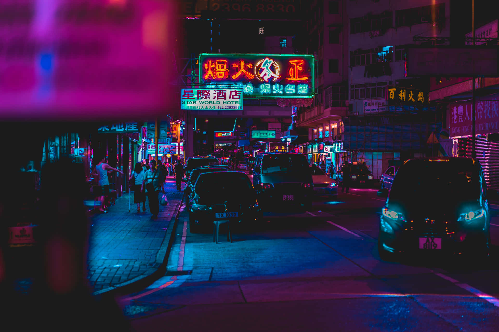 夜間霓虹燈照亮城市街道，閃爍的招牌和停放的汽車。