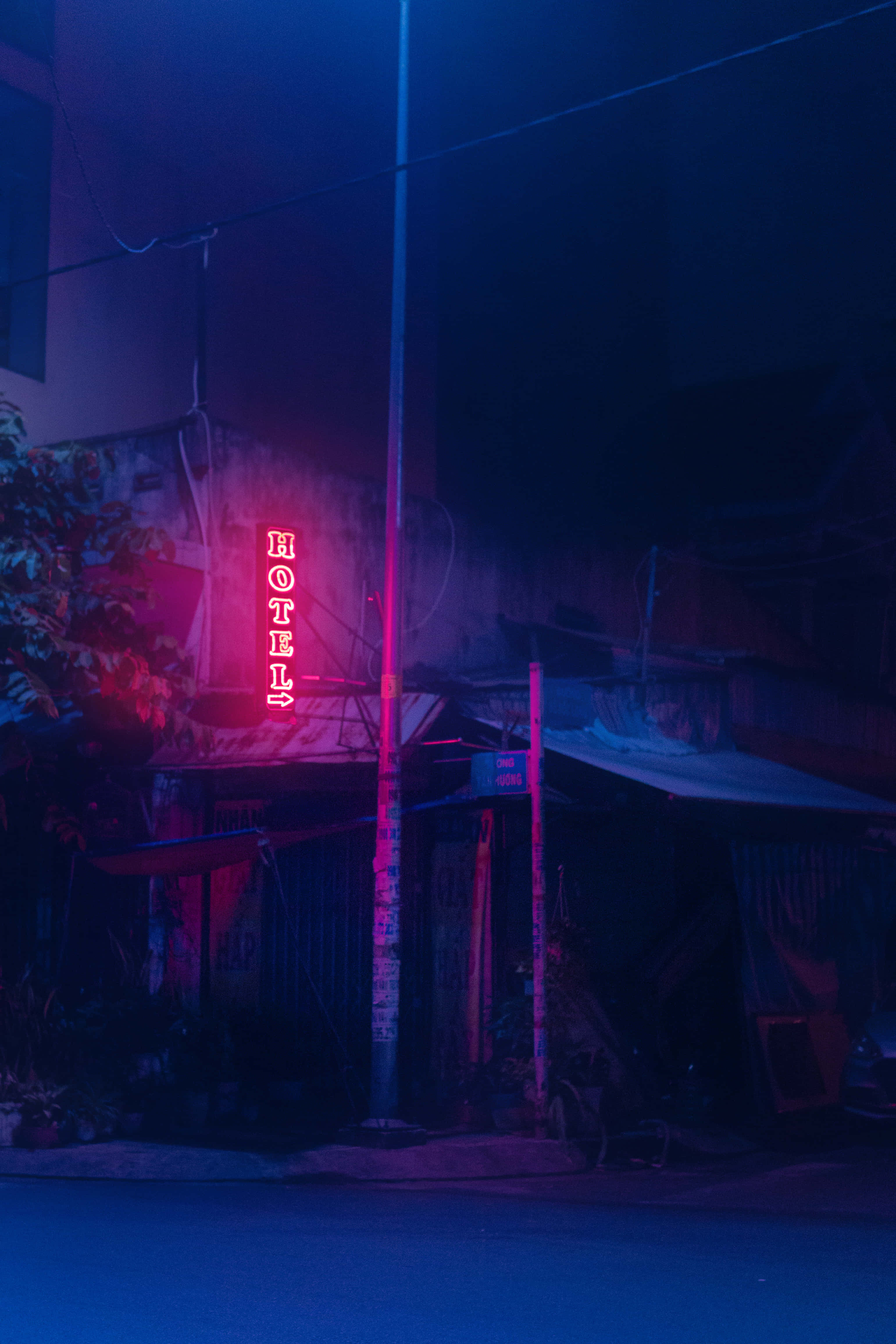 Vibes 桌布 壁紙 — 夜間，一個發光的紅色霓虹燈酒店招牌在破舊的城市小巷中投射出鮮豔的粉紅色和藍色光芒。