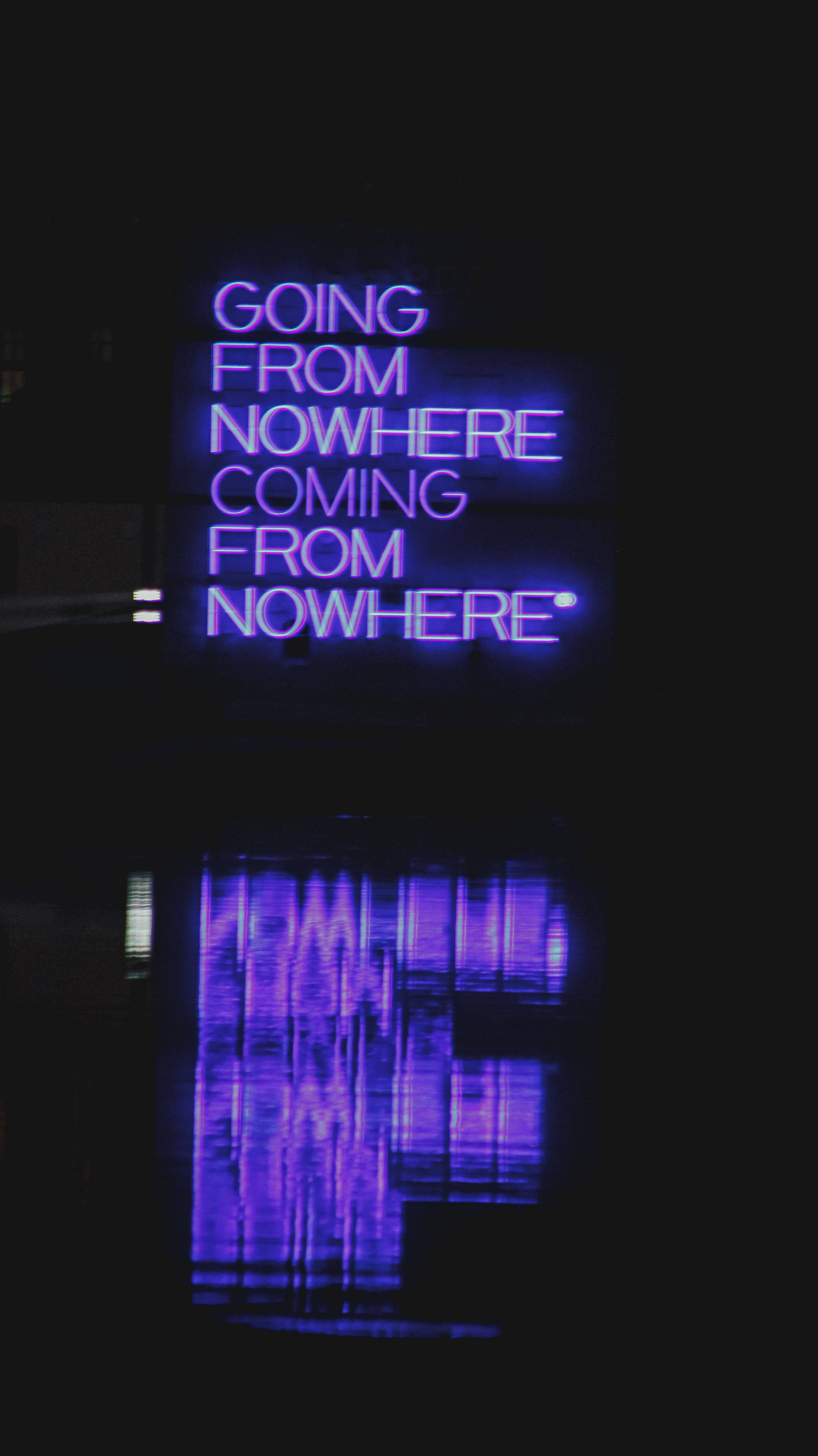 紫色 桌布 壁紙 — 夜間，一個發光的紫色霓虹燈牌，上面寫著「GOING FROM NOWHERE COMING FROM NOWHERE」，倒映在黑暗的水面上。