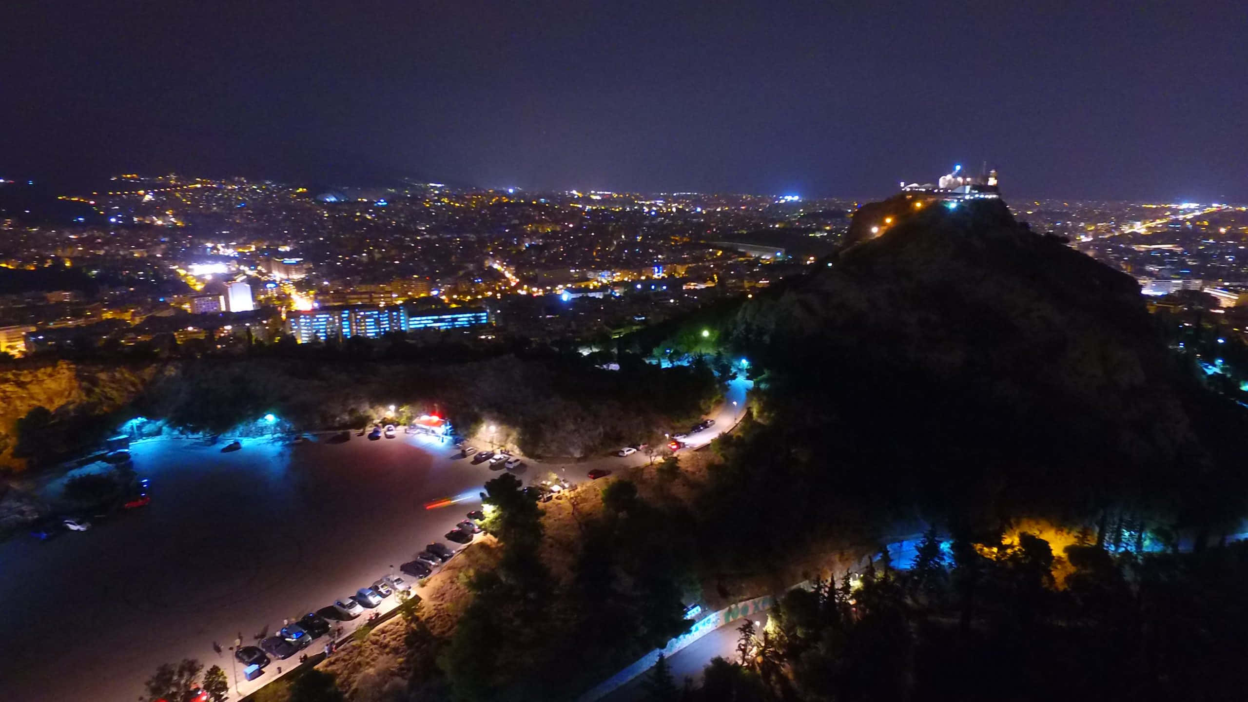 夜間利卡貝圖斯山的彩色燈光 壁紙 — 城市在燈火通明的山頂堡壘下方延伸的夜間鳥瞰圖，俯瞰著閃閃發光的海濱。