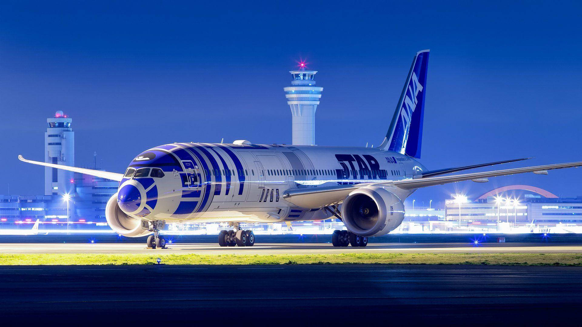 夜間機場停機坪上的R2-D2主題飛機，背景有控制塔。