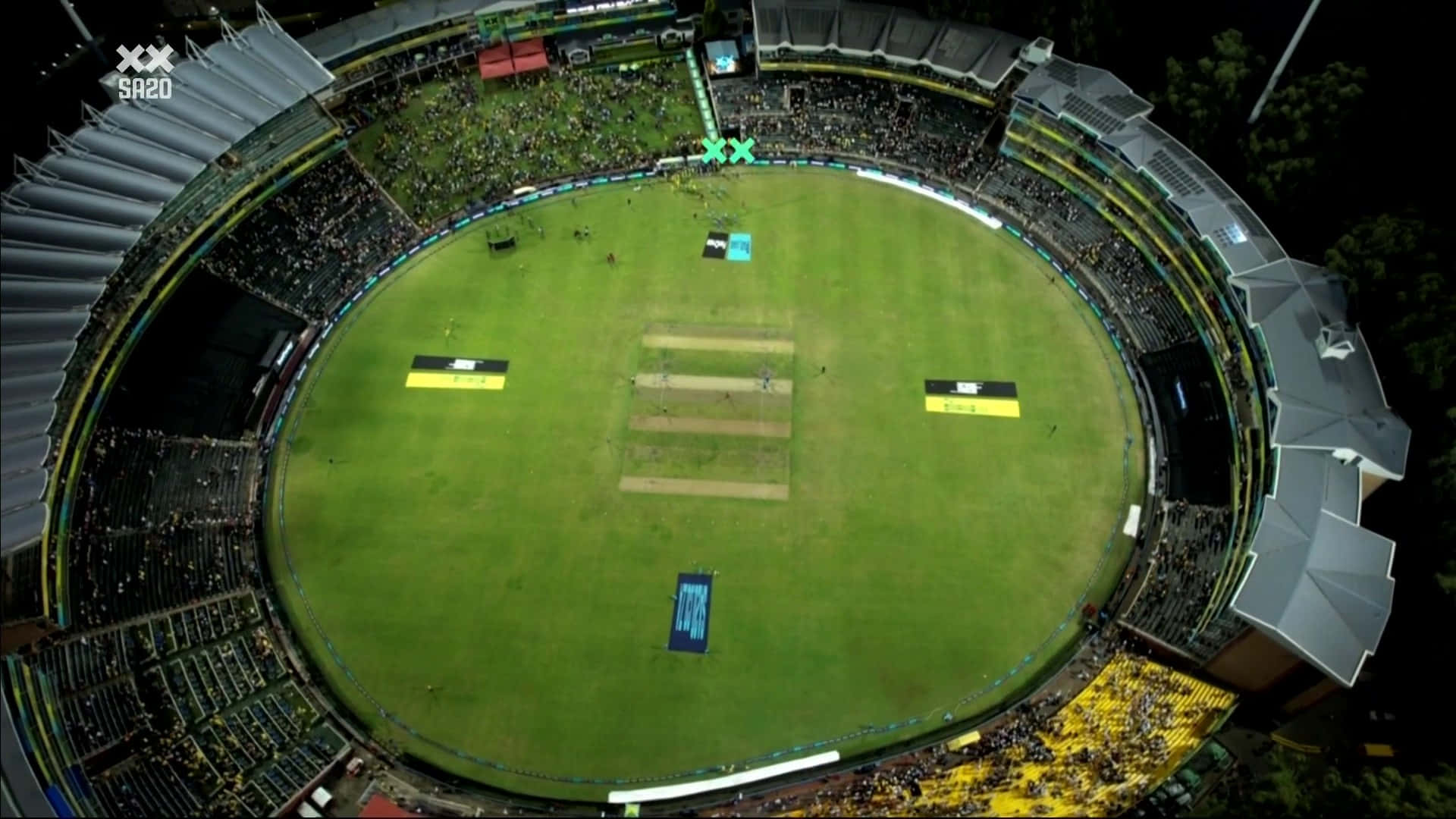 Cricket Ground 桌布 壁紙 — 夜間擠滿觀眾的板球場鳥瞰圖，發光的綠色場地和歡呼的人群。