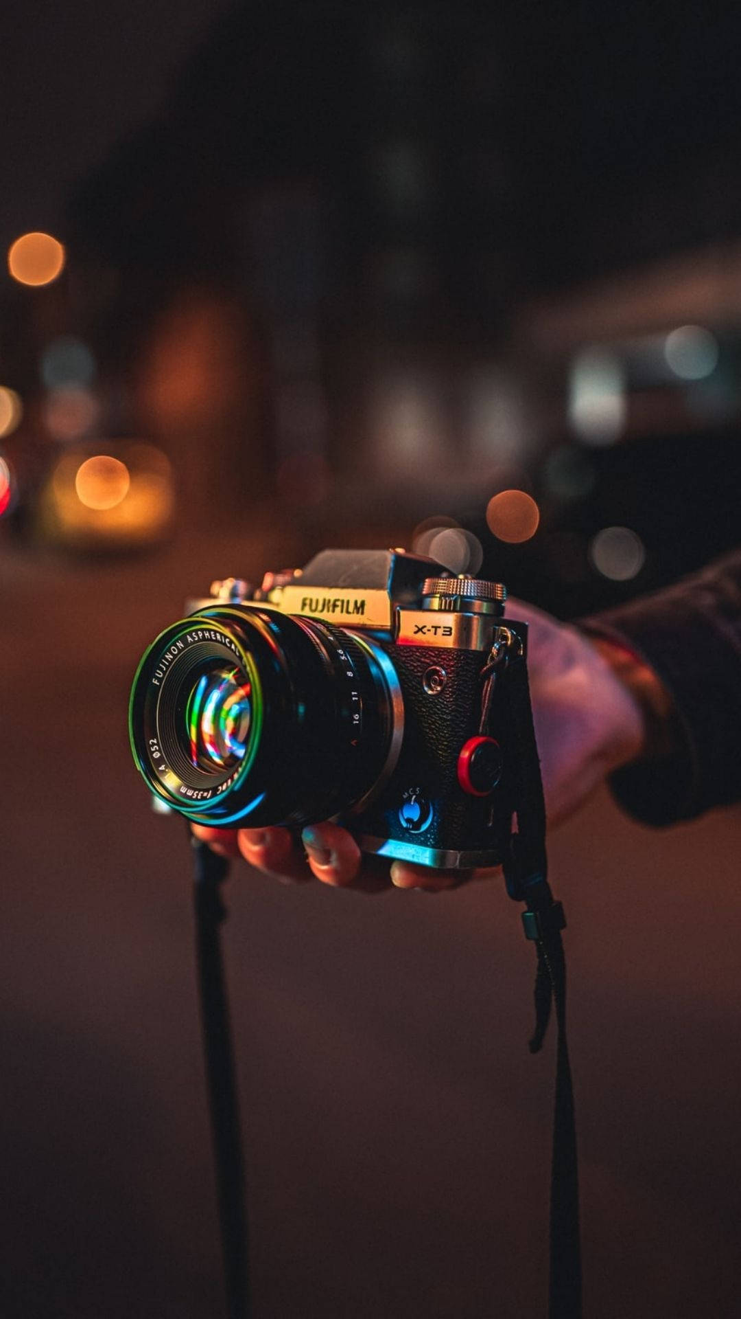 夜間攝影師 壁紙 — 夜晚手持Fujifilm X-T3相機，背景有色彩繽紛的鏡頭反射和溫暖的散景燈光。