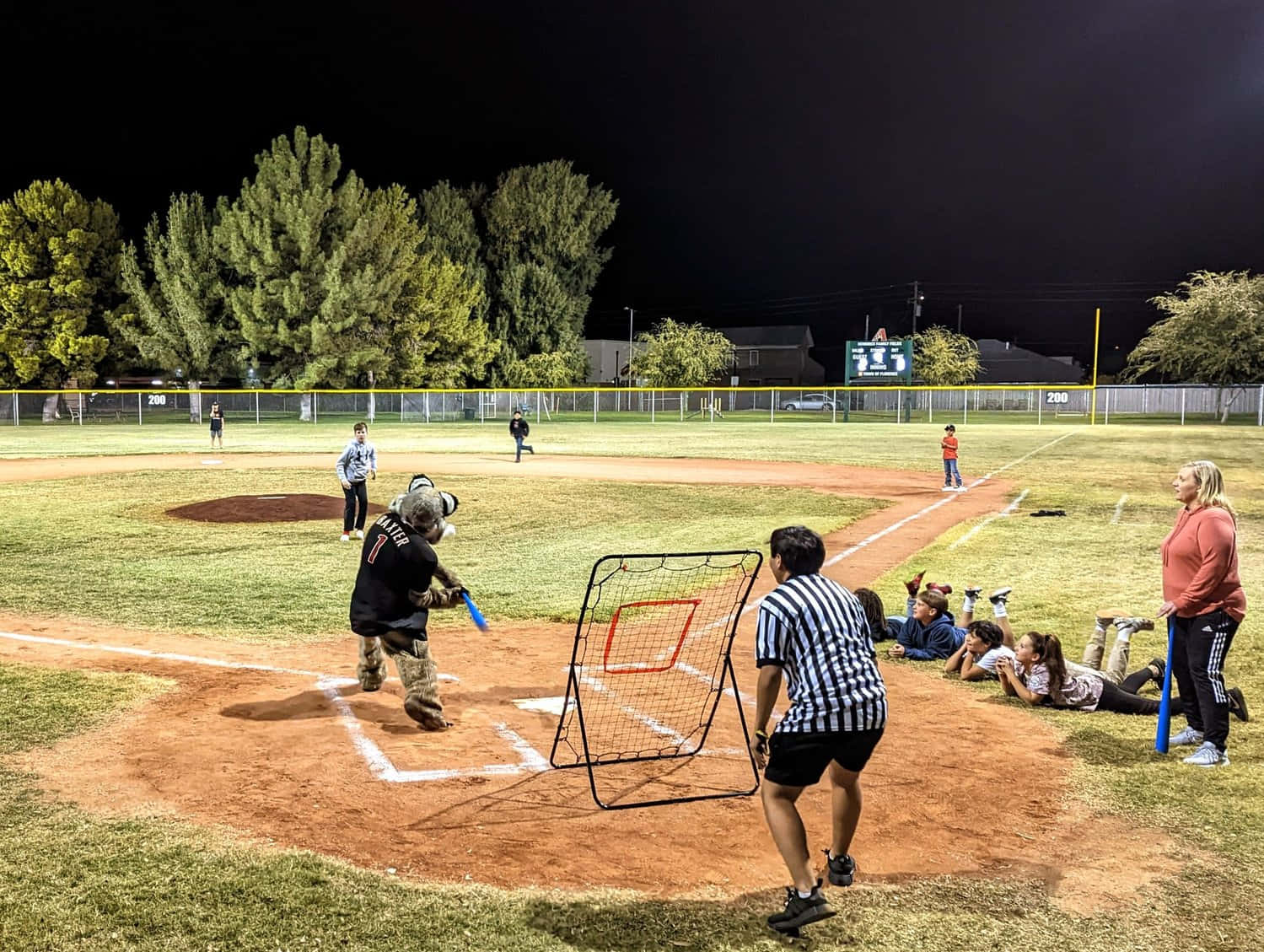 Little League Baseball 桌布 壁紙 — 夜間棒球比賽，在明亮的體育場燈光下，孩子們在打球，成年人從邊線觀看。