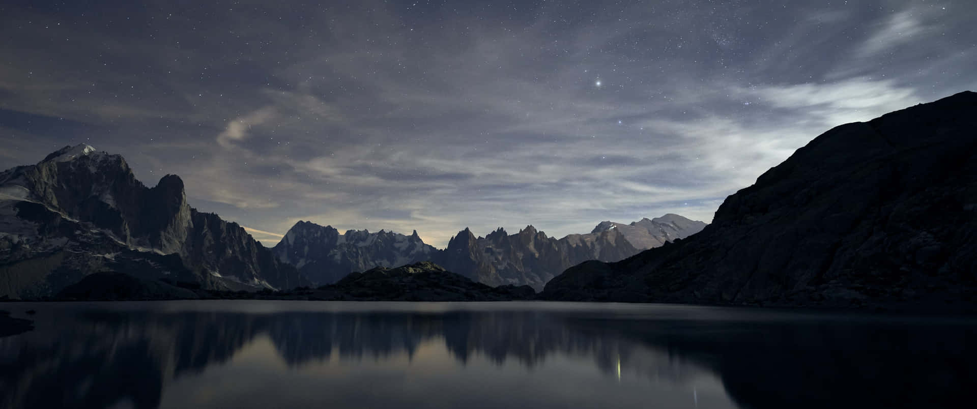 繁星點點的夜空倒映在平靜的湖中，背景是鋸齒狀的山脈。