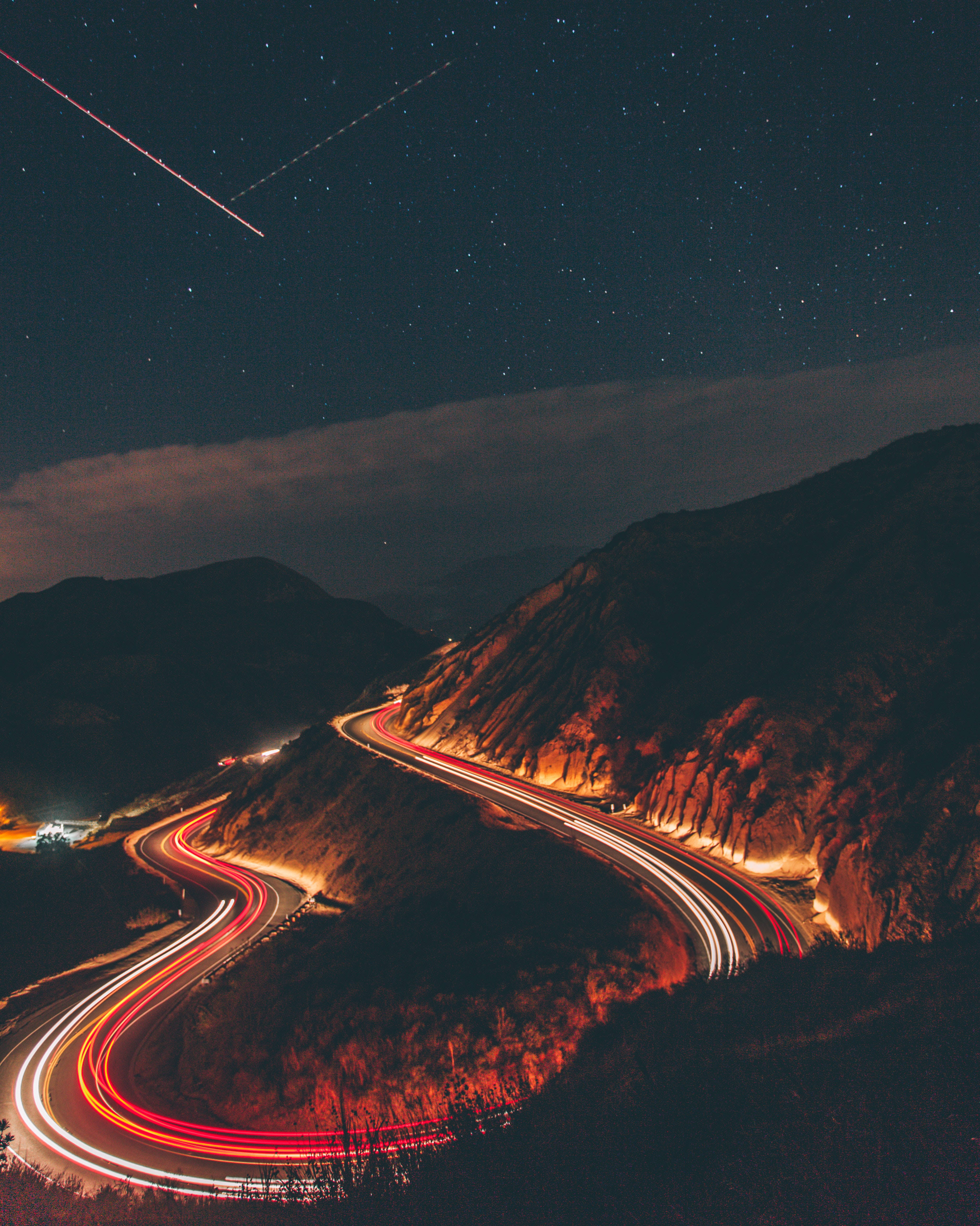 夜間燈光軌跡 壁紙 — 夜晚蜿蜒的山路在星空下閃爍著汽車的紅色和白色光軌，還有一顆流星。