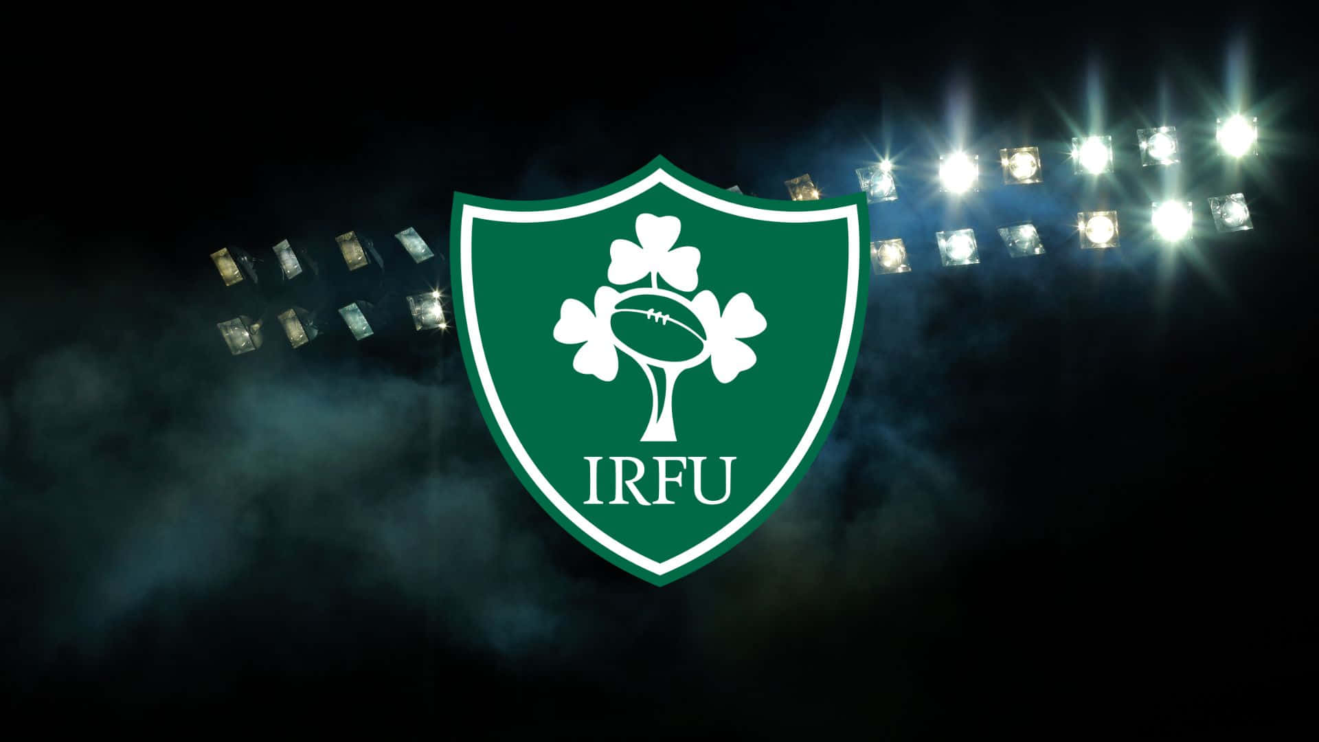 Ireland Rugby 桌布 壁紙 — 夜間球場燈光下，一個發光的綠色IRFU盾牌，中央有酢漿草和欖球。